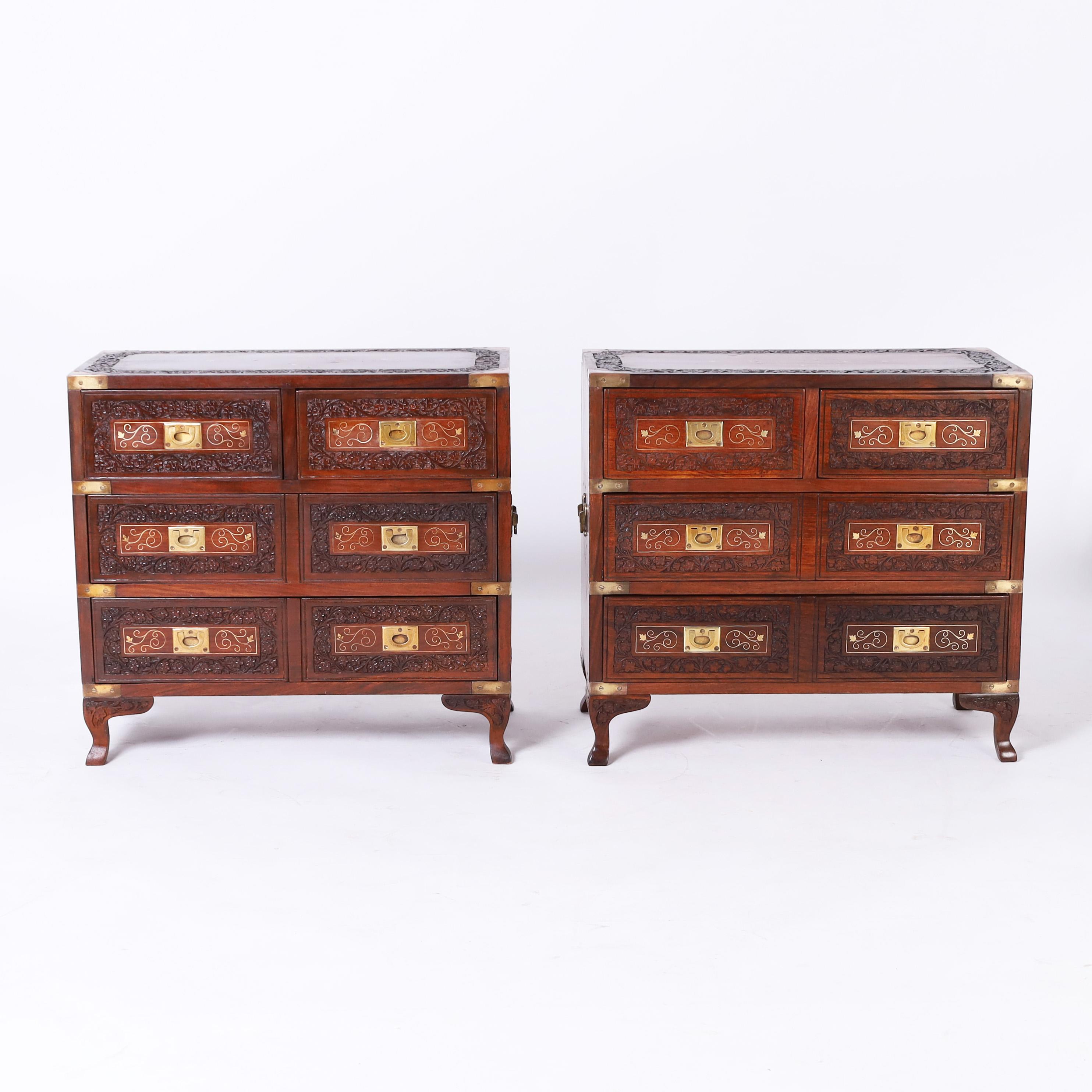 Impressive near pair of Anglo Indian campaign stands featuring tops with floral brass string inlaid medallions inside a carved border over a case having four drawers with brass inlays and carved floral borders, brass campaign hardware, side handles