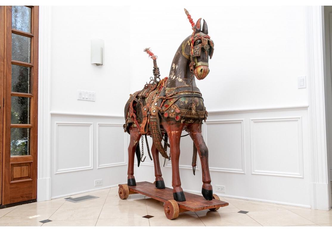 An Exceptional Indian Folk Art Temple Horse. A nearly life size horse figure carved and painted brown with painted and gilt decoration on the body with roundels, floral bands, and red and black patterns. With elaborate trappings and saddle in