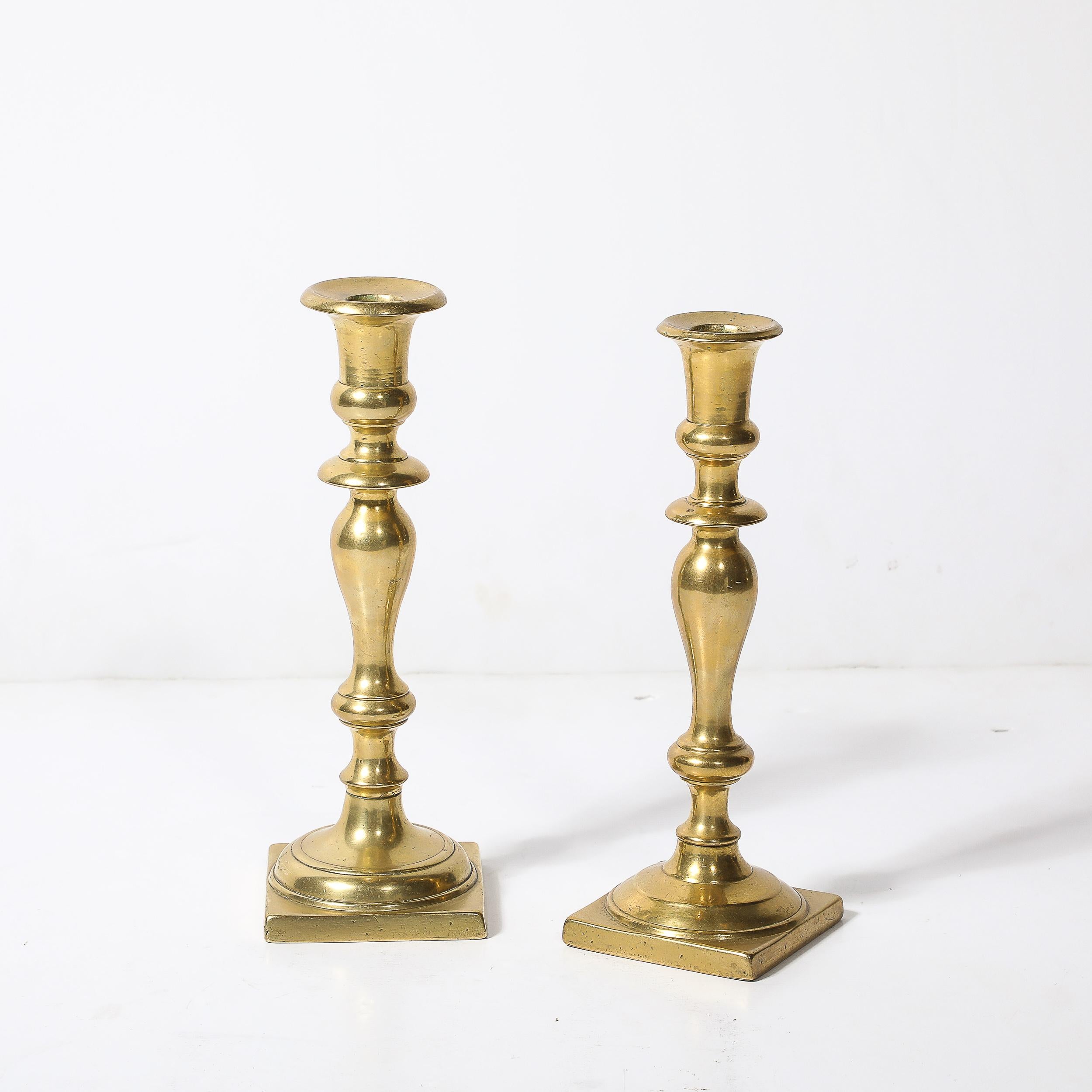 Questa elegante coppia di portacandele neoclassici, realizzata negli Stati Uniti, risale al 1900 circa.  Questi modelli mostrano il fascino senza tempo dell'ottone lucido combinato con elementi di design classico. Ogni portacandela presenta una base