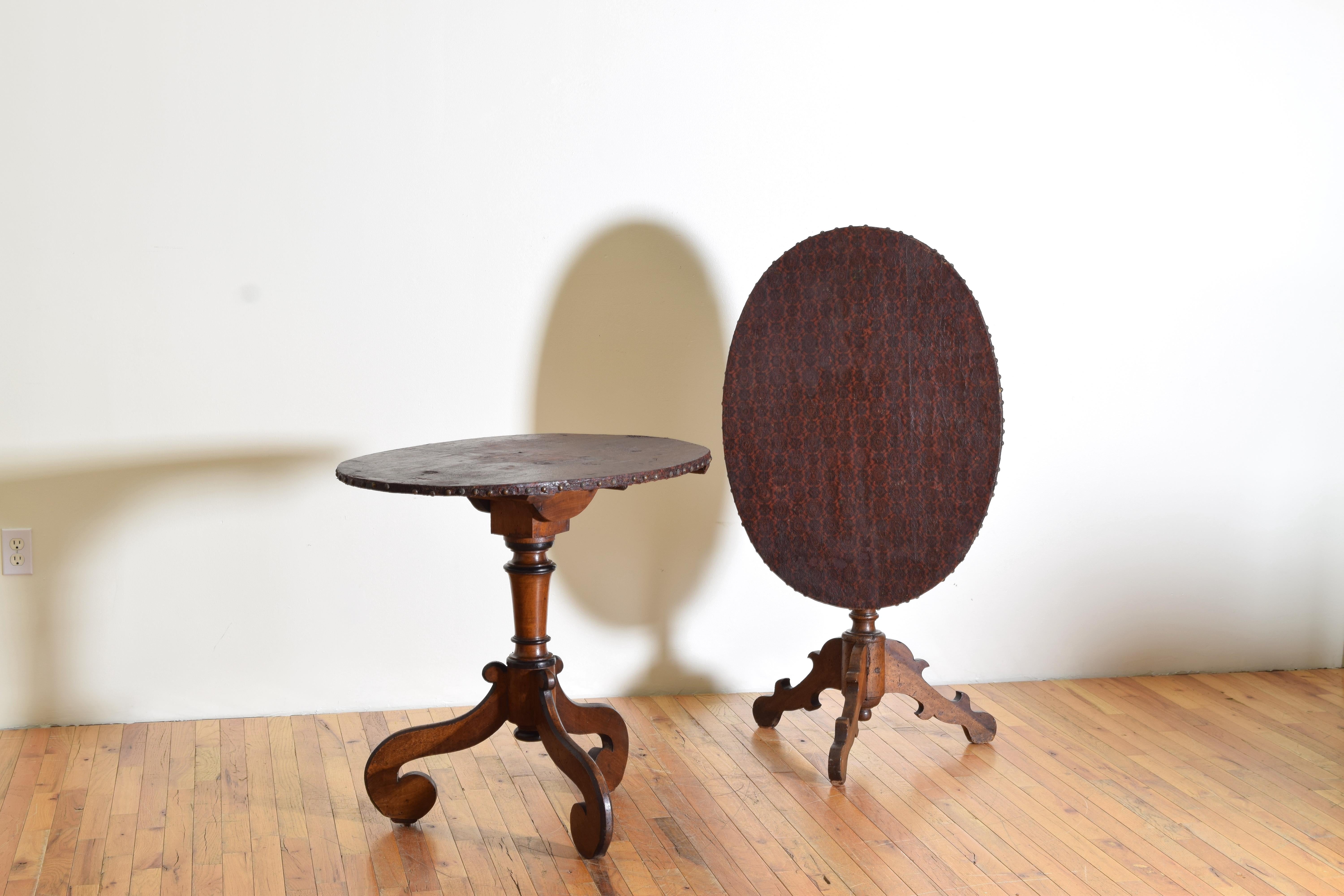Each table having a tilting oval top covered in pattern embossed and dyed canvas, the tops above square supports and having removable wooden pins to secure them in upright position, raised on turned standards each issuing three legs of slightly