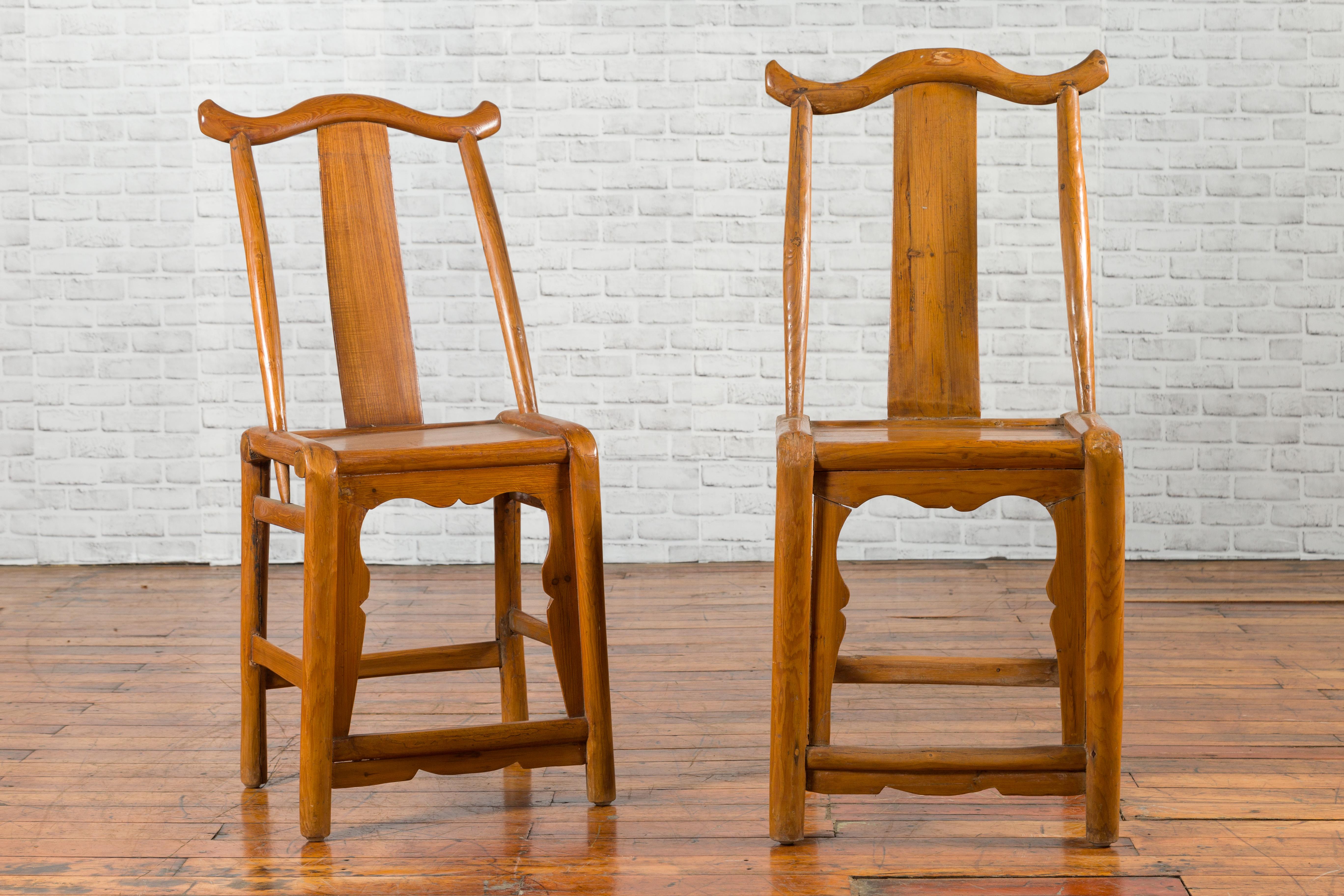 A near pair of Chinese Qing dynasty period yoke high back chairs from the 19th century, with carved aprons and side stretchers. Created in China during the Qing dynasty and showcasing slightly different dimensions, each of this near pair of