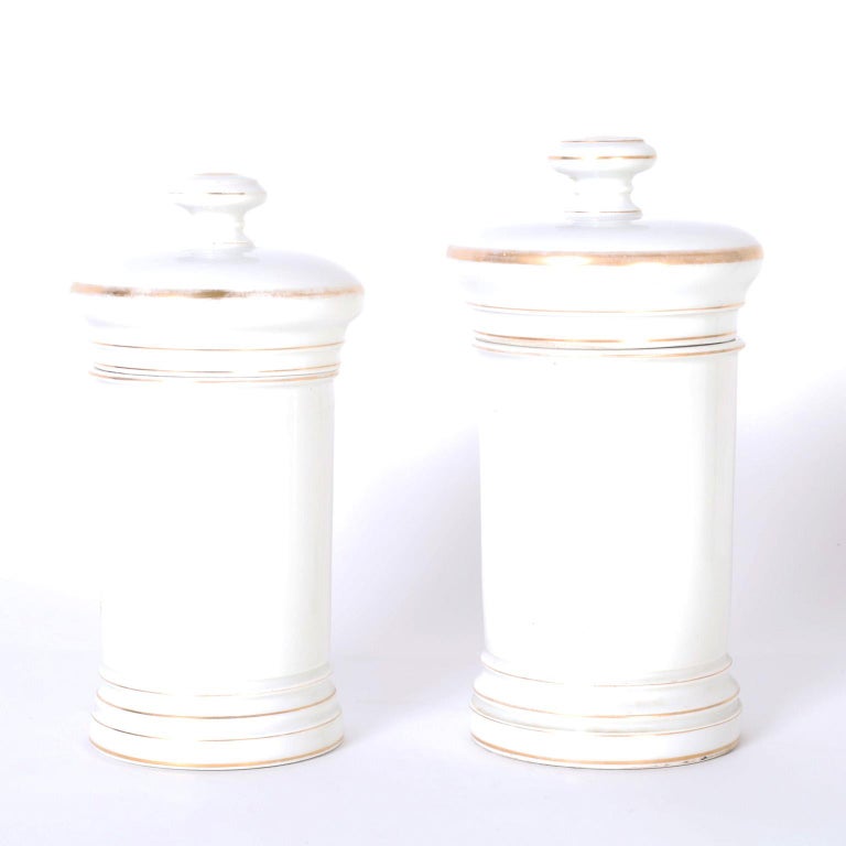 Two matching porcelain apothecary jars with classic form hand decorated with intriguing colorful medical symbols with palm trees.

From left to right:

H: 10 DM: 5

H: 11 DM: 5.5.