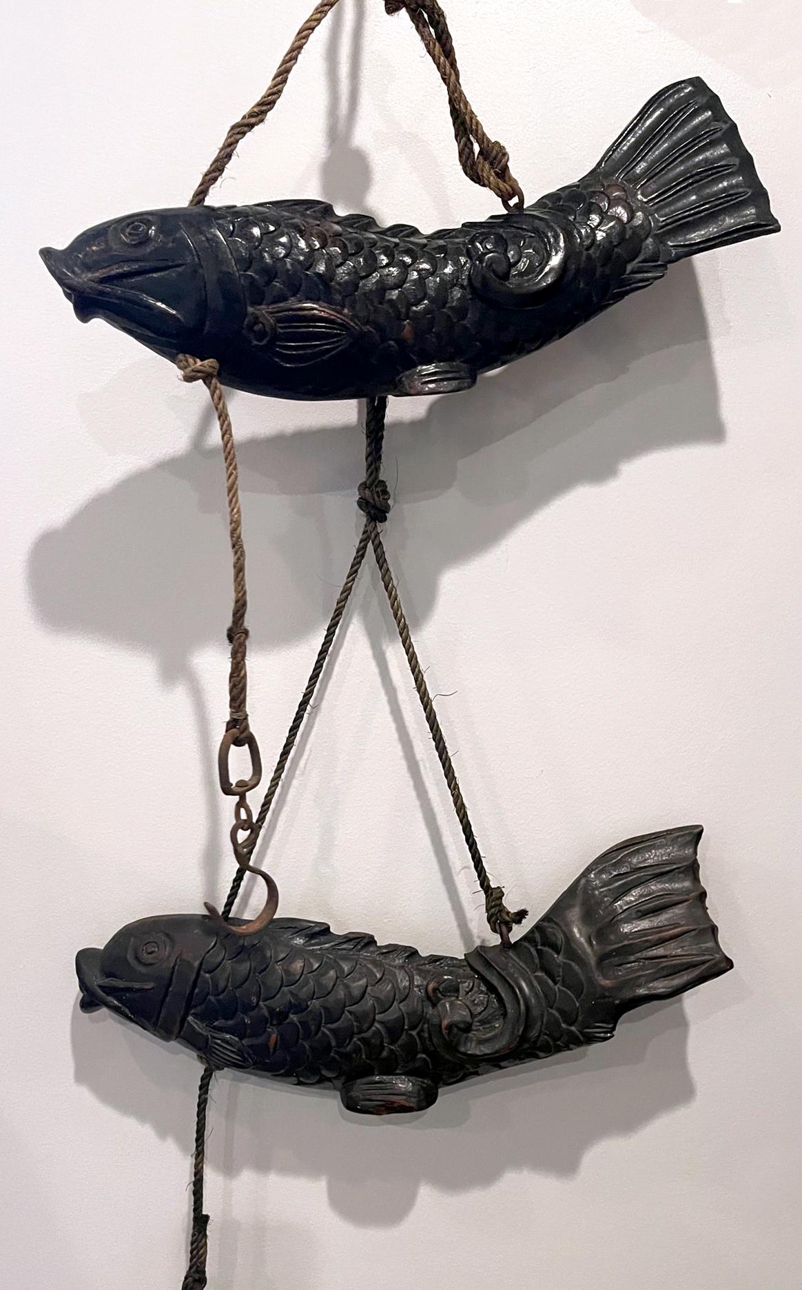 A near pair of wood koi fish from Japan circa 1860-90s of late Meiji Period. Hand-carved from solid wood, these sculptures are known as Jizai Kagi in Japanese and function as the leveling pulley for the attached hearth hook. Traditionally, they were