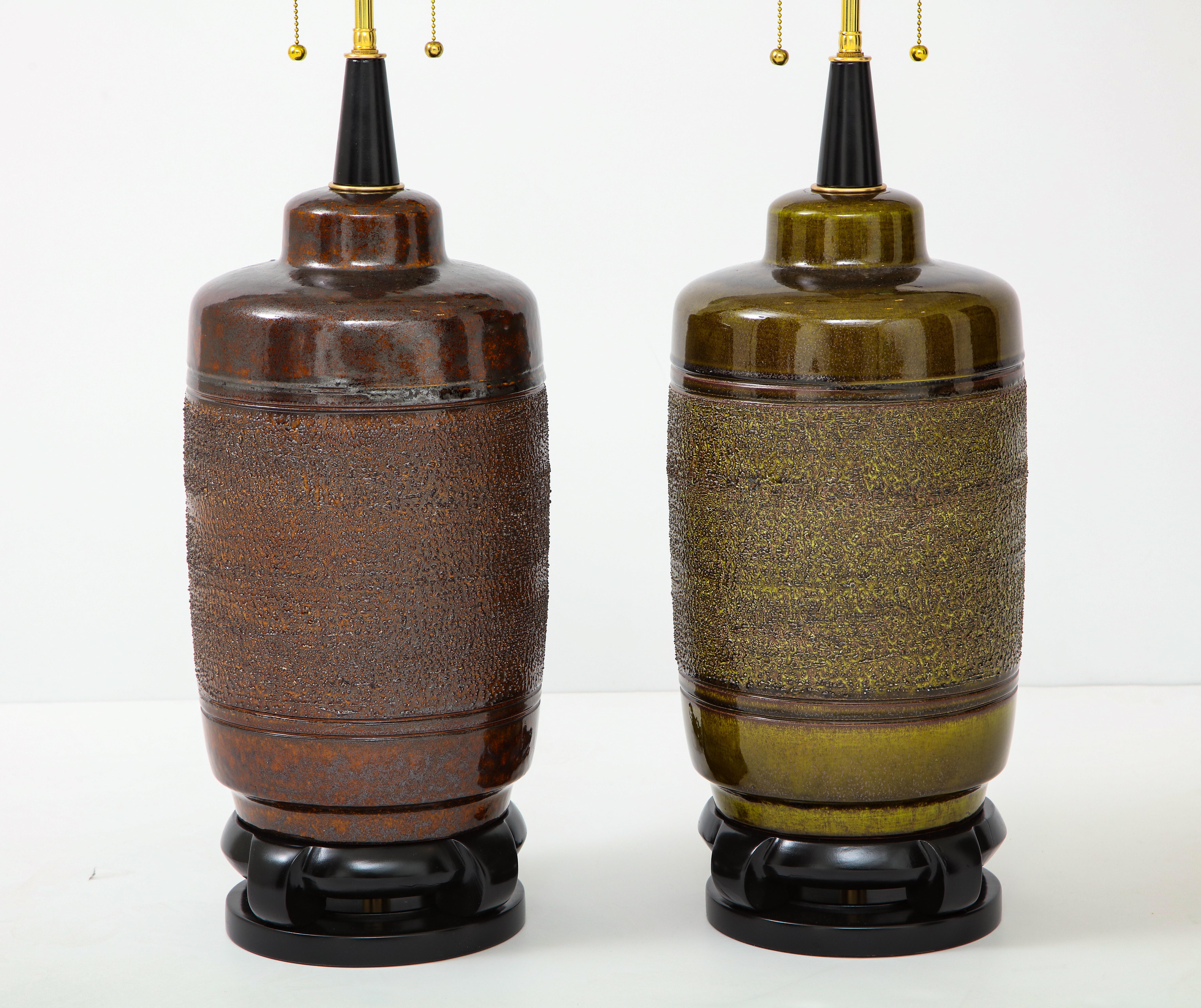 Large near matched pair of ceramic lamps by Paul Hanson.
The large ceramic lamp bodies have a textured glazed finish.
One lamp has a moss green glaze and the other a brown glaze.
The lamps have been newly rewired with polished brass double