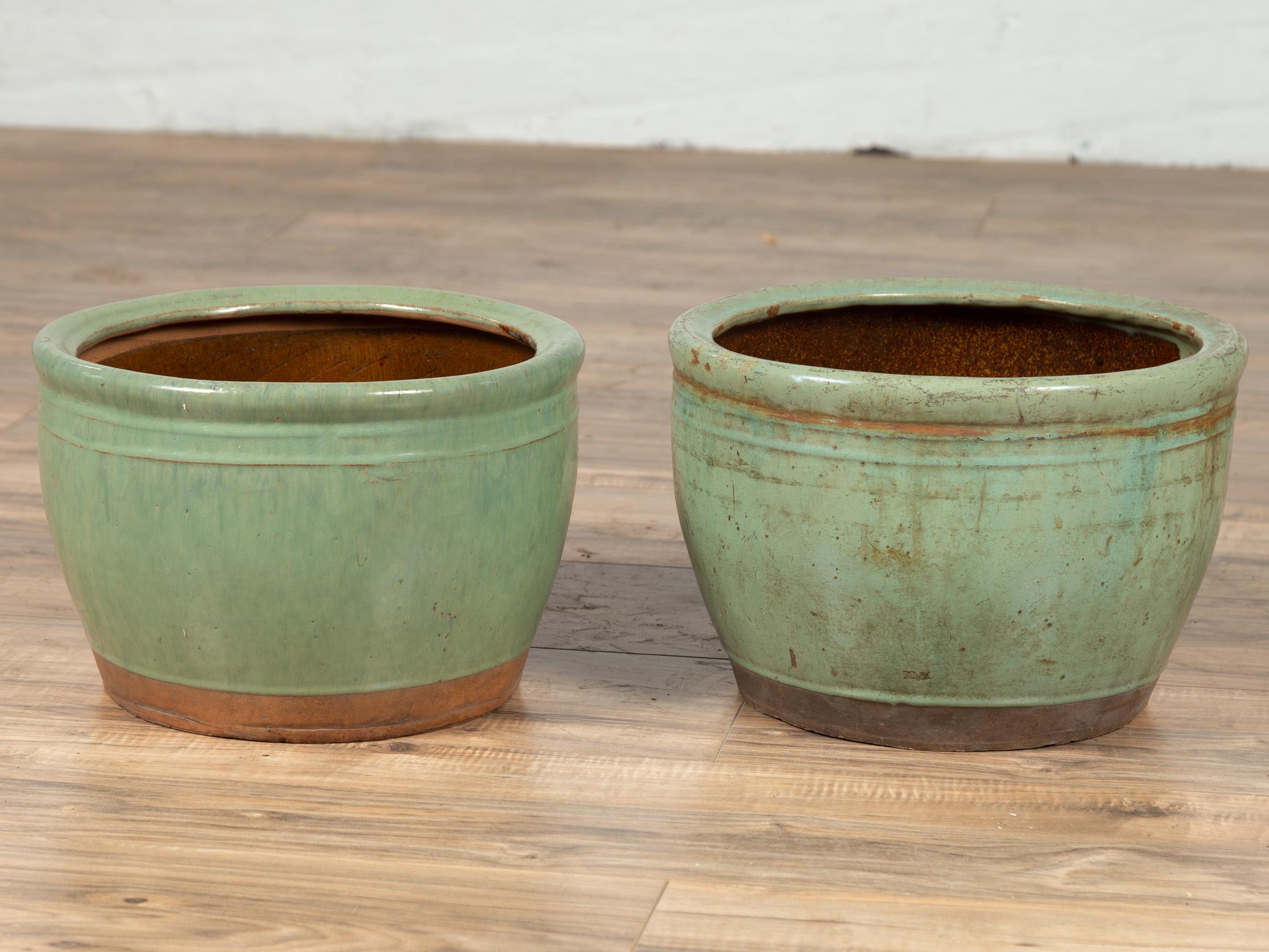 A vintage near pair of Chinese large ceramic planters from the mid-20th century, with soft green glazed finish. Born in China during the midcentury period, each of this pair of large planters features a circular tapering body, accented by a lovely
