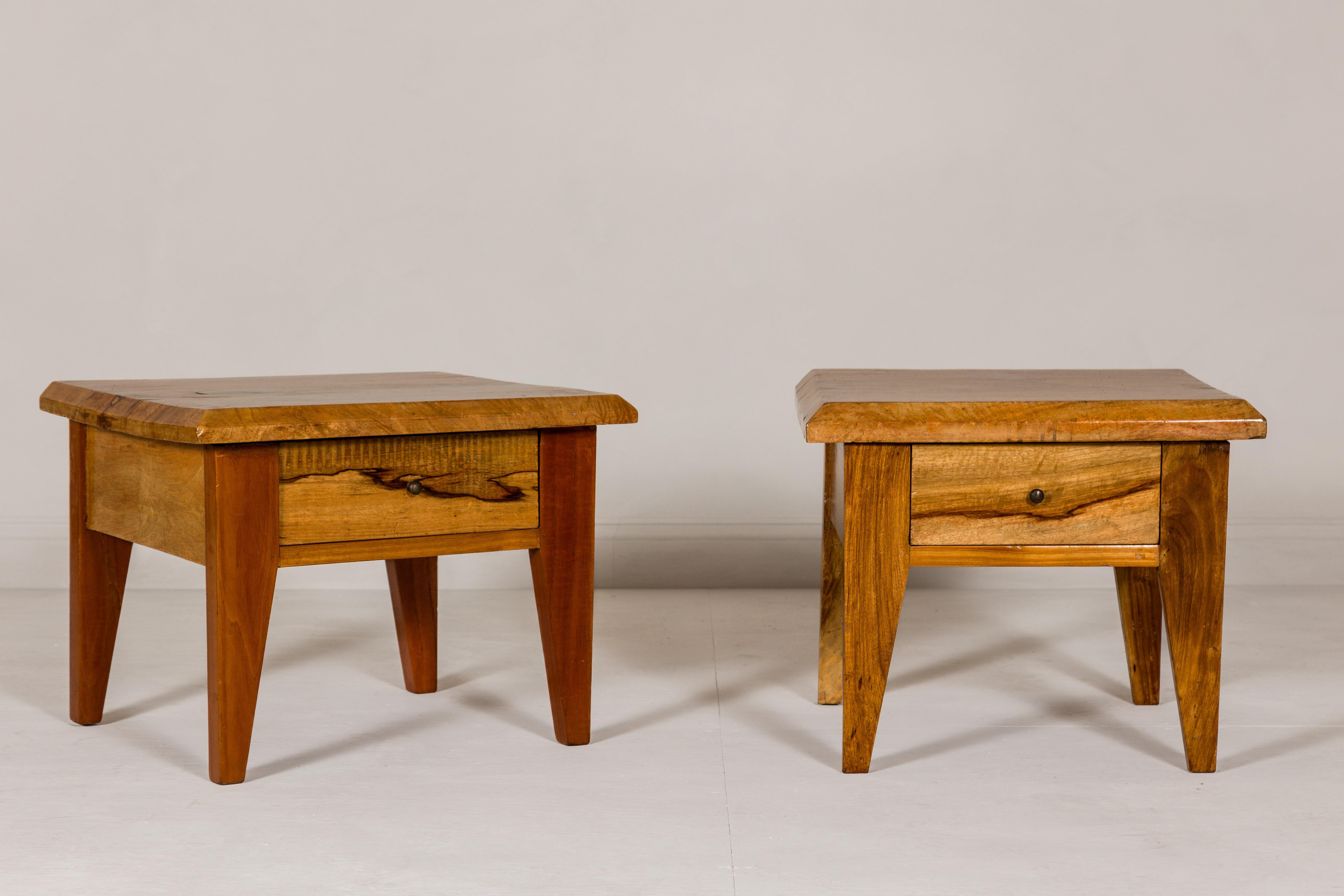 A near pair of Midcentury mango wood low side tables with single drawers and tapering legs. Embodying the timeless appeal of Midcentury design, this near pair of low side tables combines the rich texture of mango wood with functional elegance. The