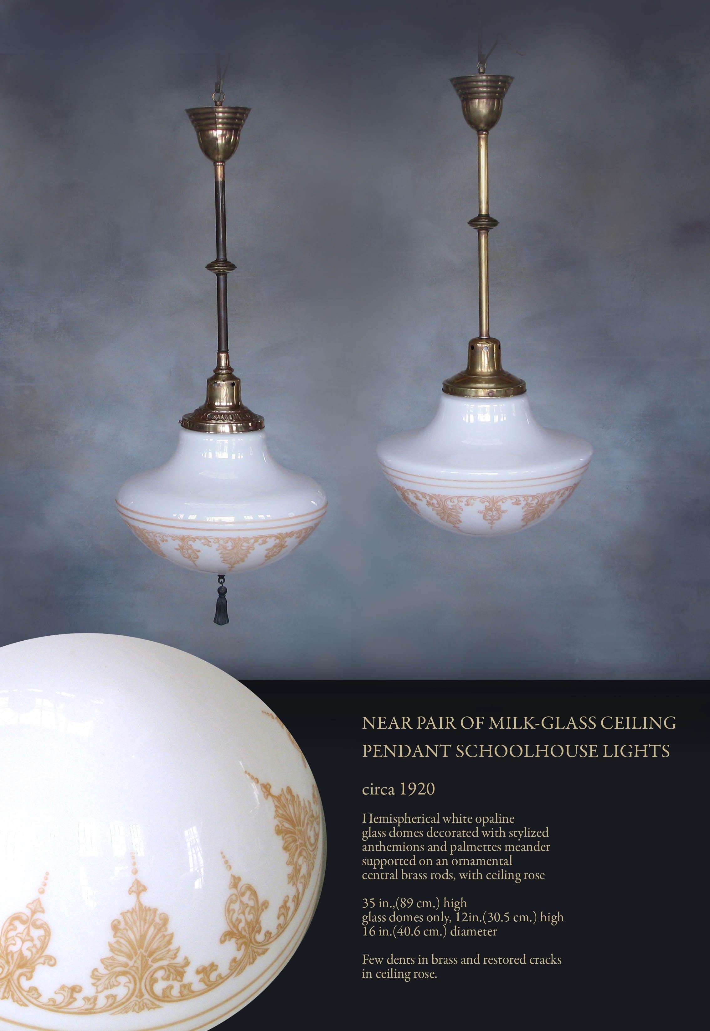 Near pair of milk-glass ceiling
pendant schoolhouse lights

Circa 1920.

Hemispherical white opaline
glass domes decorated with stylized
anthemions and palmettes meander
supported on an ornamental
central brass rods, with ceiling