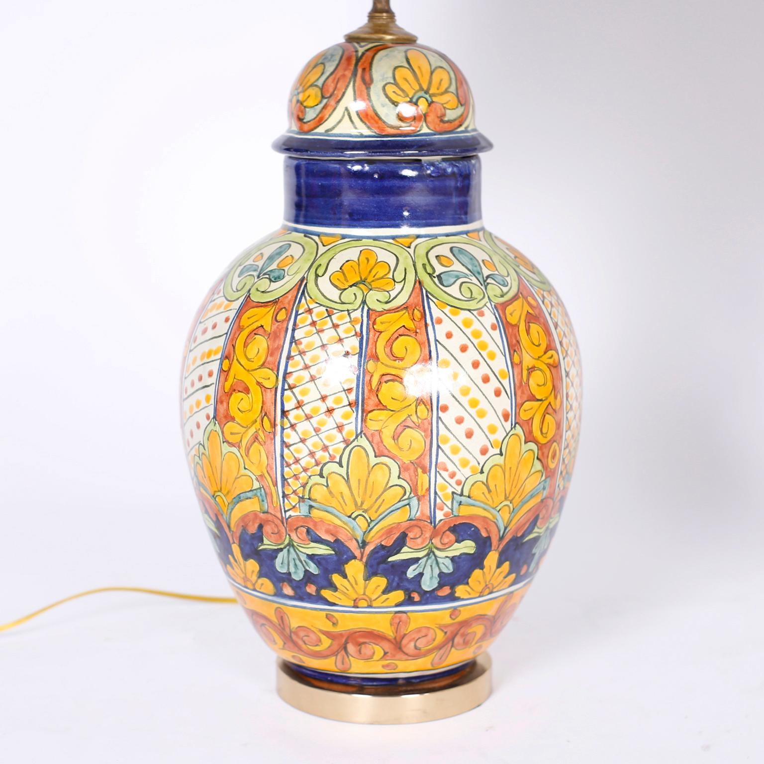 Near pair of table lamps crafted in terracotta with a classic urn form hand decorated under glaze with floral designs in distinctive Mediterranean colors presented on brass bases.