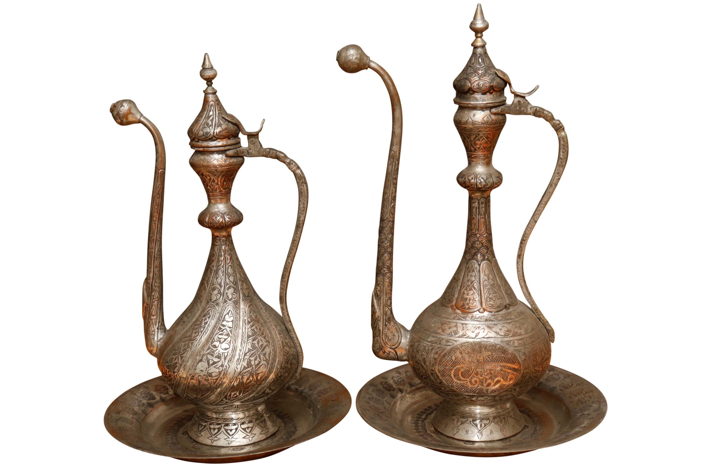 A near pair of large Middle Eastern silver plated copper ewers with matching plates. Tall ewers and plates are ornately engraved throughout with a vine like motif. Ewers measure 12