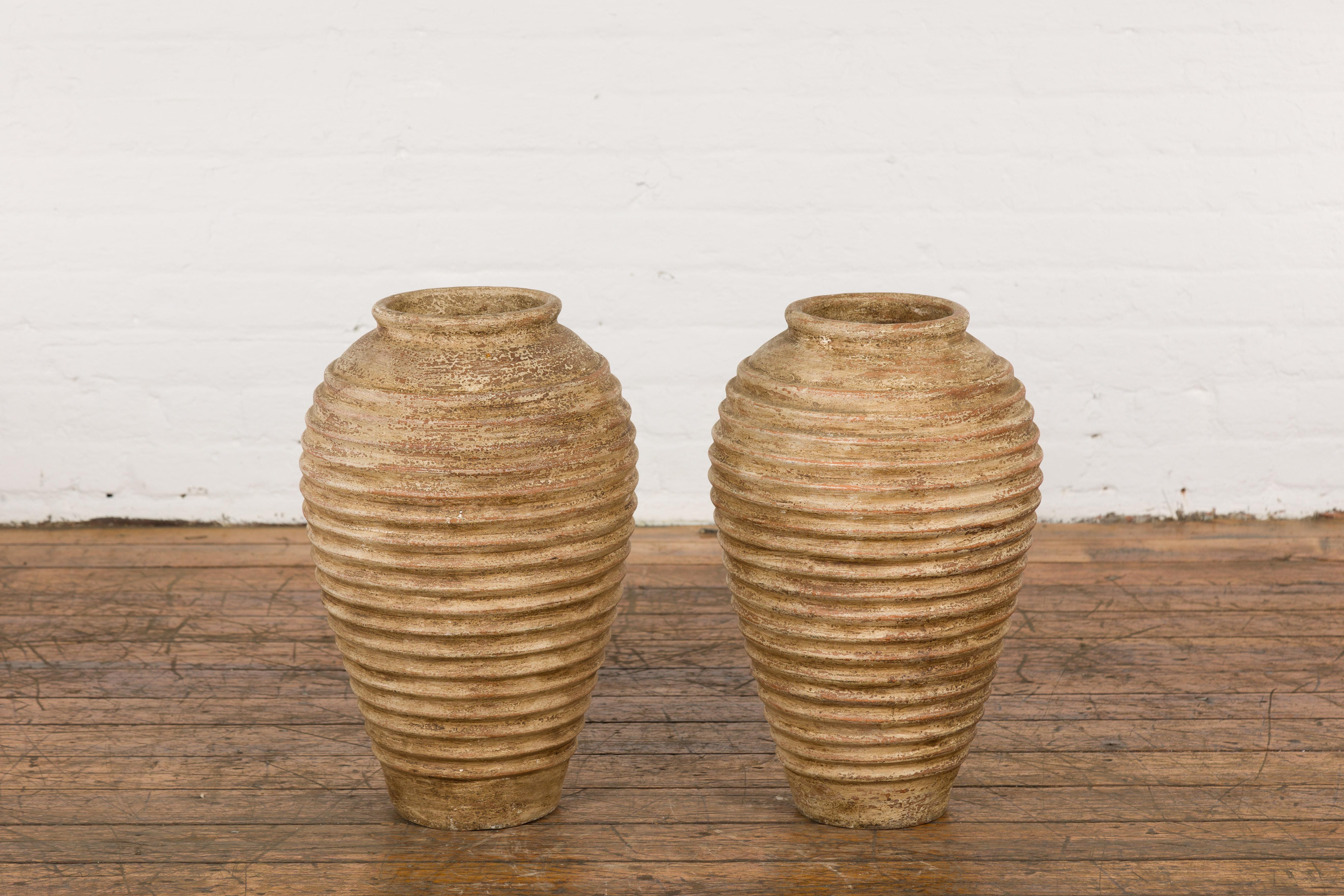 A near pair of vintage Thai storage vases from the mid 20th century with concentric circle design, rustic character and distressed patina. Exude a sense of rustic charm with this near pair of vintage Thai storage vases, an embodiment of traditional