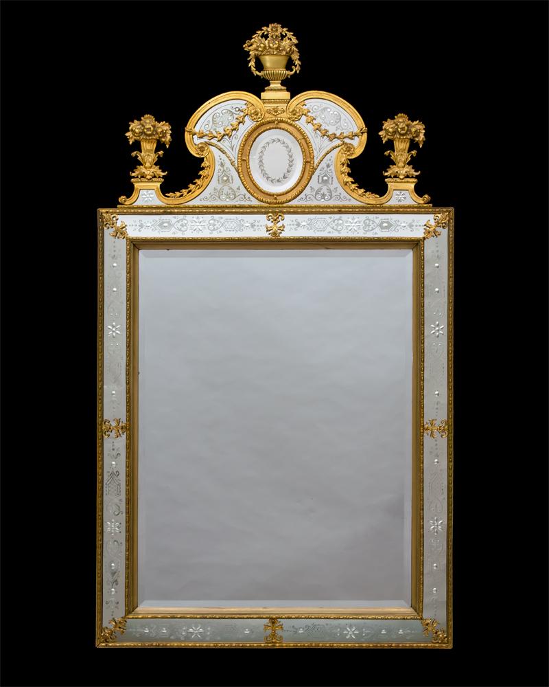Die rechteckige Spiegelplatte mit abgeschrägtem Rand ist von gravierten Tafeln im venezianischen Stil eingefasst, die mit einer Perlenbordüre aus Ormolu verziert sind. Der obere Teil ist mit einer Ormolu-Rollendekoration versehen, die mit einem