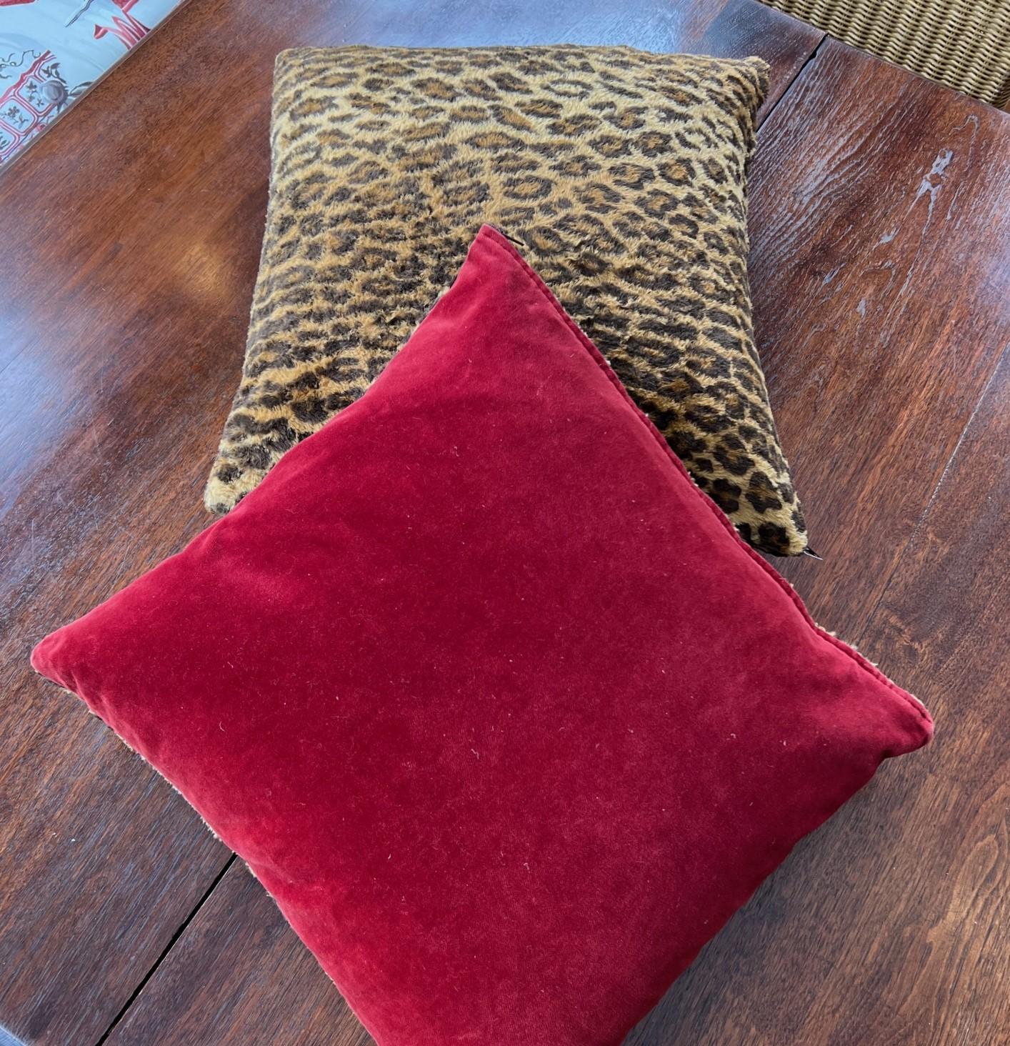 A near pair of square vintage Ralph Lauren leopard print faux fur pillows, one with a contrasting red velvet back. Both have goose feather and down inserts accessed via a zipper on the covers. The covers have a knife edge