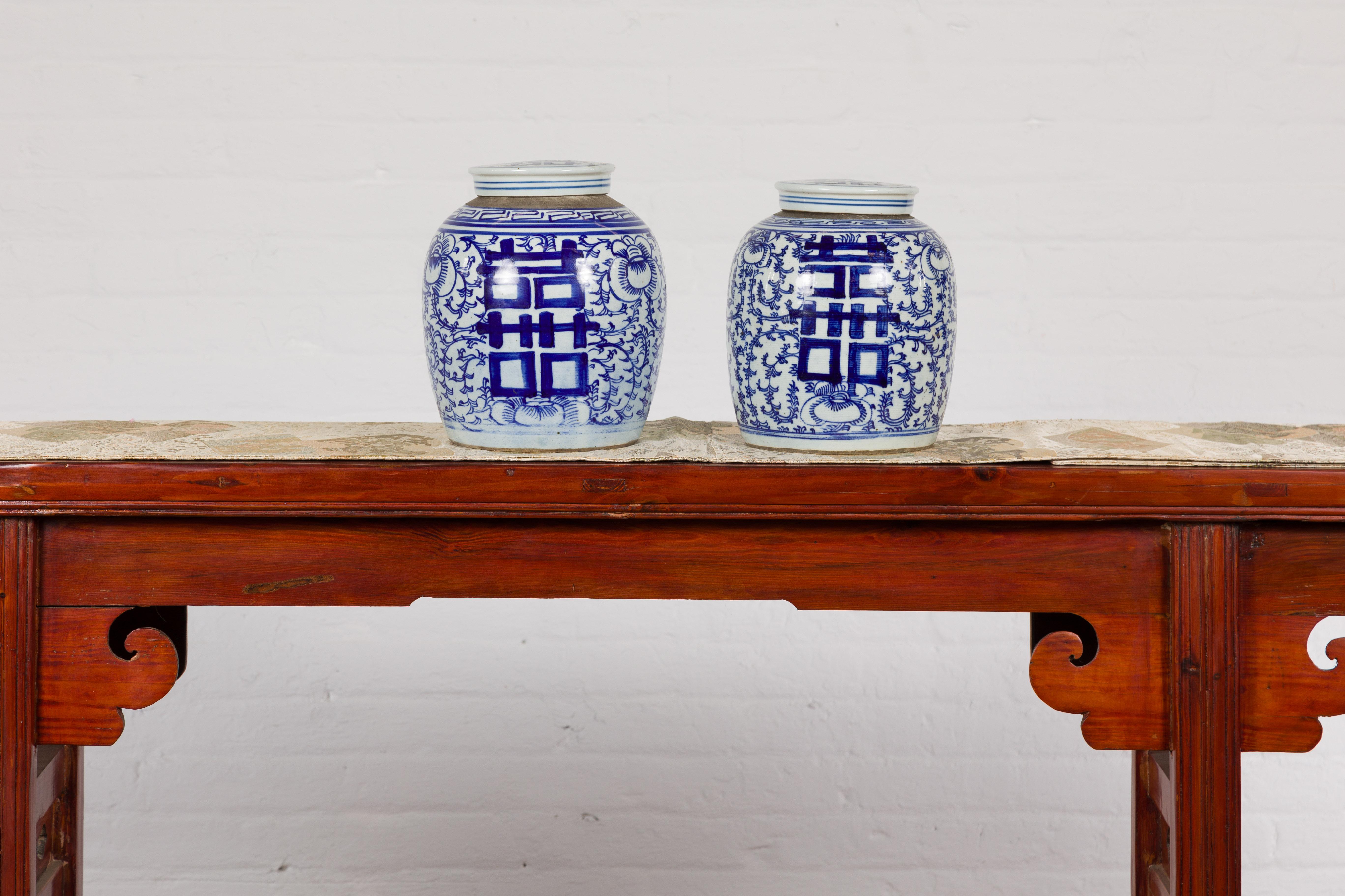 A near pair of Chinese lidded blue and white porcelain ginger jars from the mid 20th century with double happiness signs on scrolling foliage. Emanating elegance and harmony, this near pair of Chinese blue and white porcelain ginger jars from the