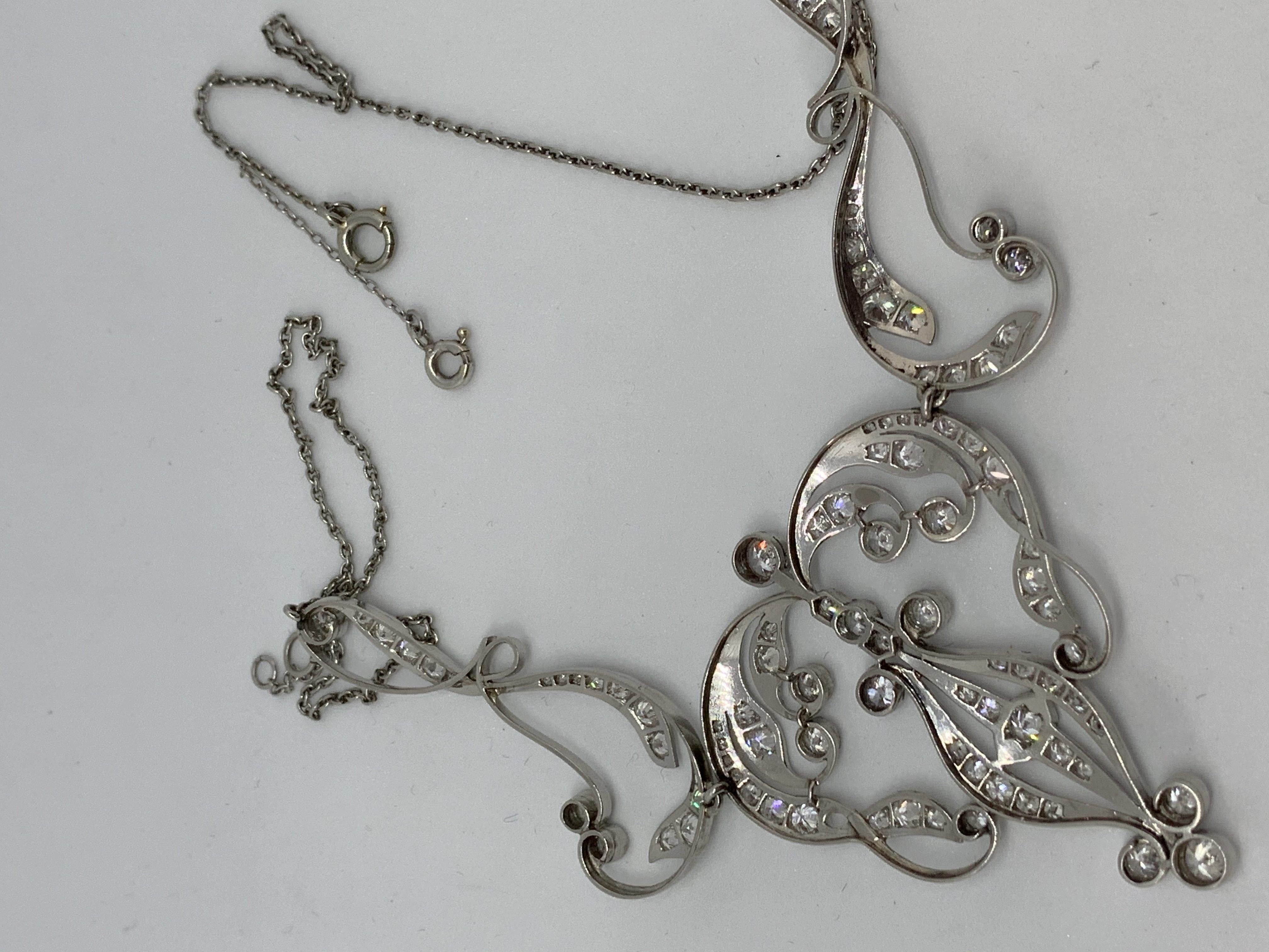 An early 20th Century three-part necklace having stylised heart centre panel between two long scrolls all suspended at the centre of a trace link chain. The wing panels of the necklace contain twenty-six diamonds totalling  .95cts.
The centre panel
