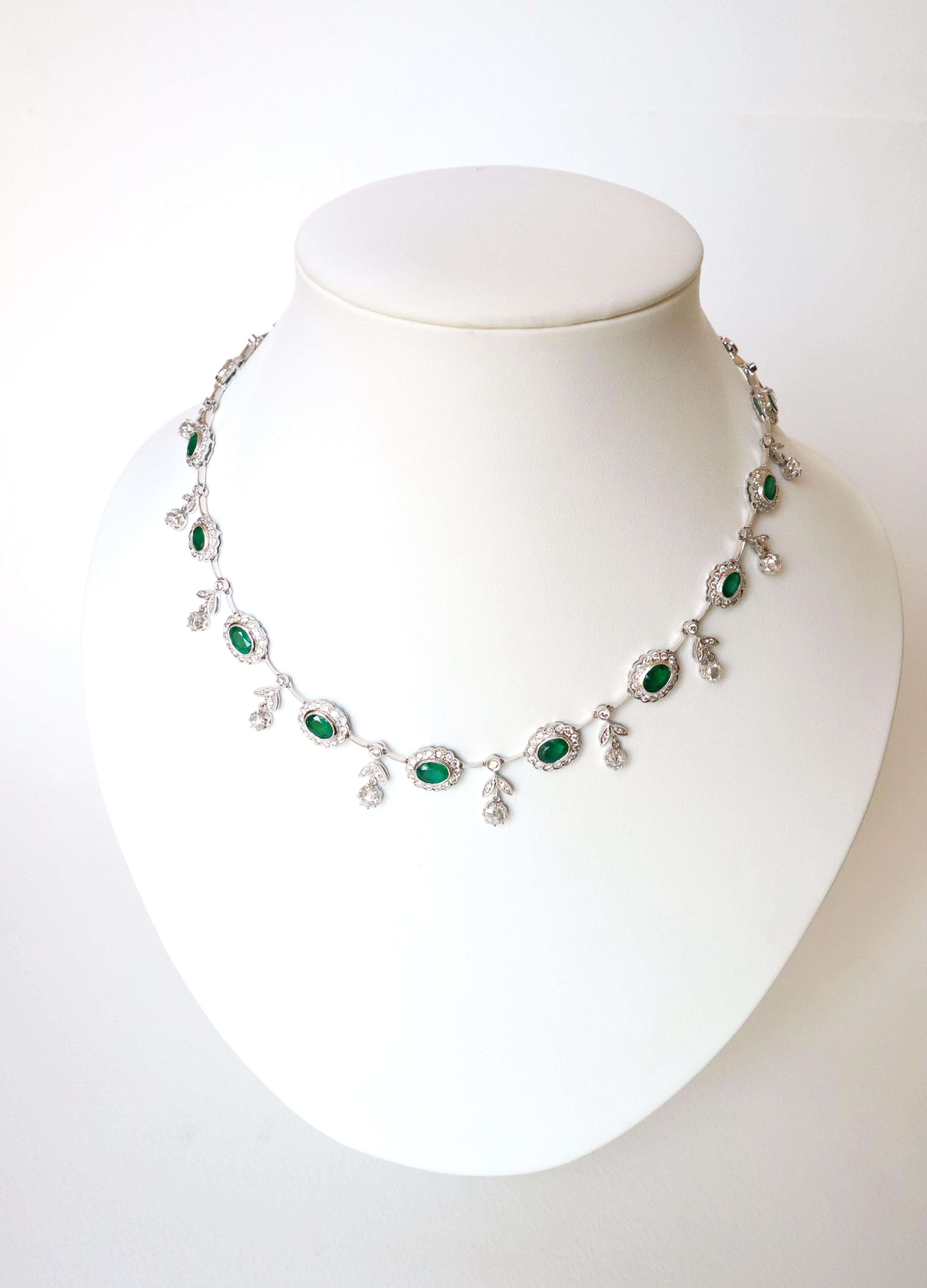 Drapery necklace in 18 karat white gold, emeralds and diamonds. It is made up of 17 pompadour motifs, each closed setting an emerald surrounded by diamonds. The motifs are linked together by 2 finely chiseled articulated rods linked together by a