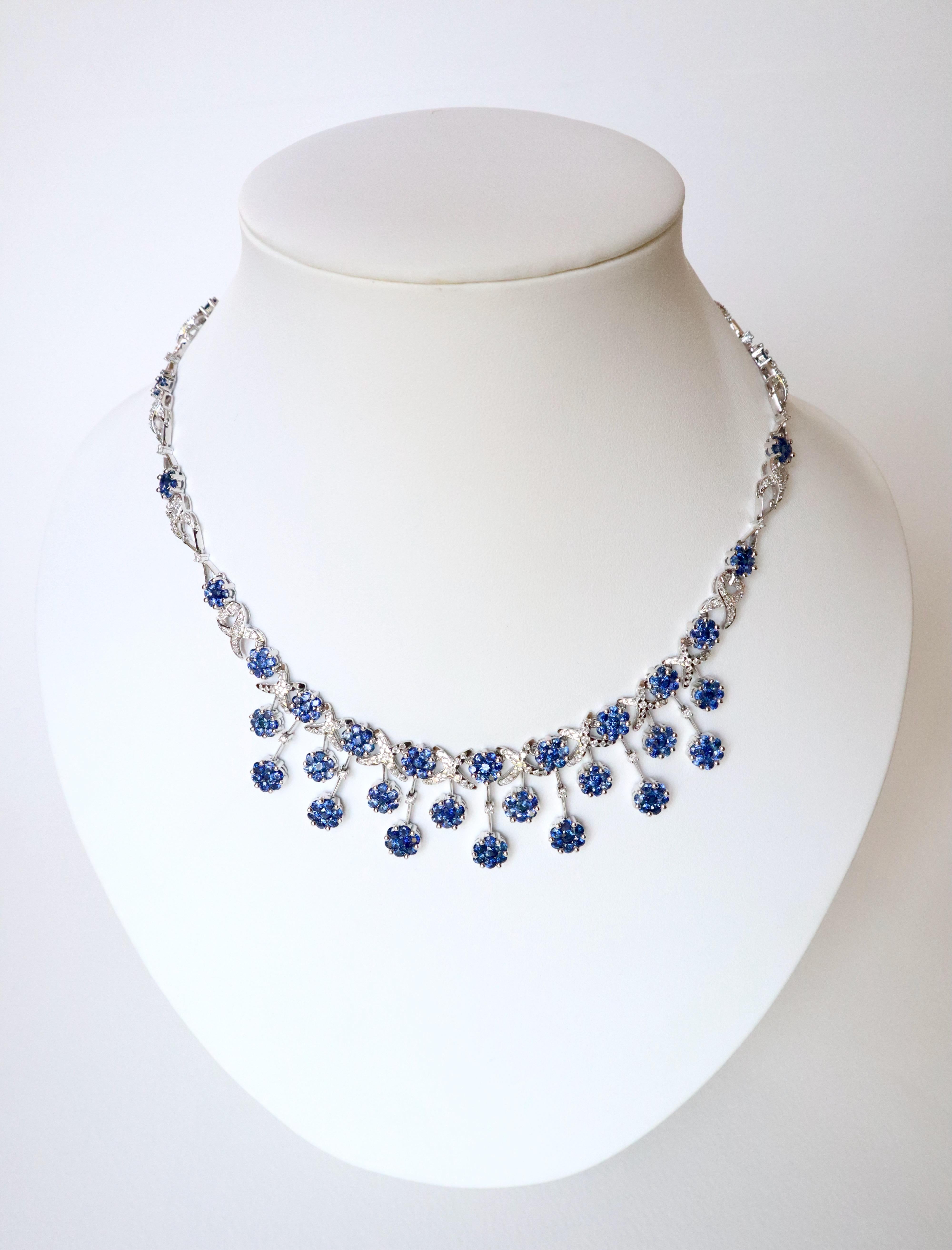 Drapery necklace in 18 carat white gold, sapphires and diamonds. It is composed of 21 floral motifs composed of 7 sapphires each held together by interlaced links paved with diamonds or by chains. The center of the necklace is made up of 15 floral