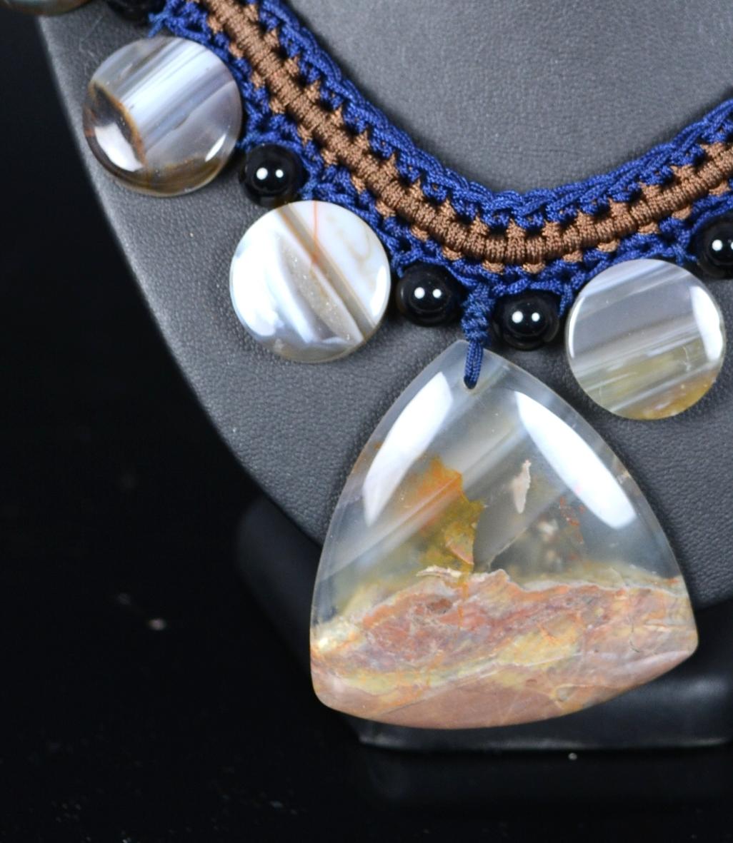 Halskette mit mexikanischen Achatplatten.
Halskette aus Schnüren in verschiedenen Farbtönen, dank derer die Perlen, aus denen sie besteht, platziert und hervorgehoben werden: flache runde Scheiben wechseln sich mit dunklen kugelförmigen Perlen ab,