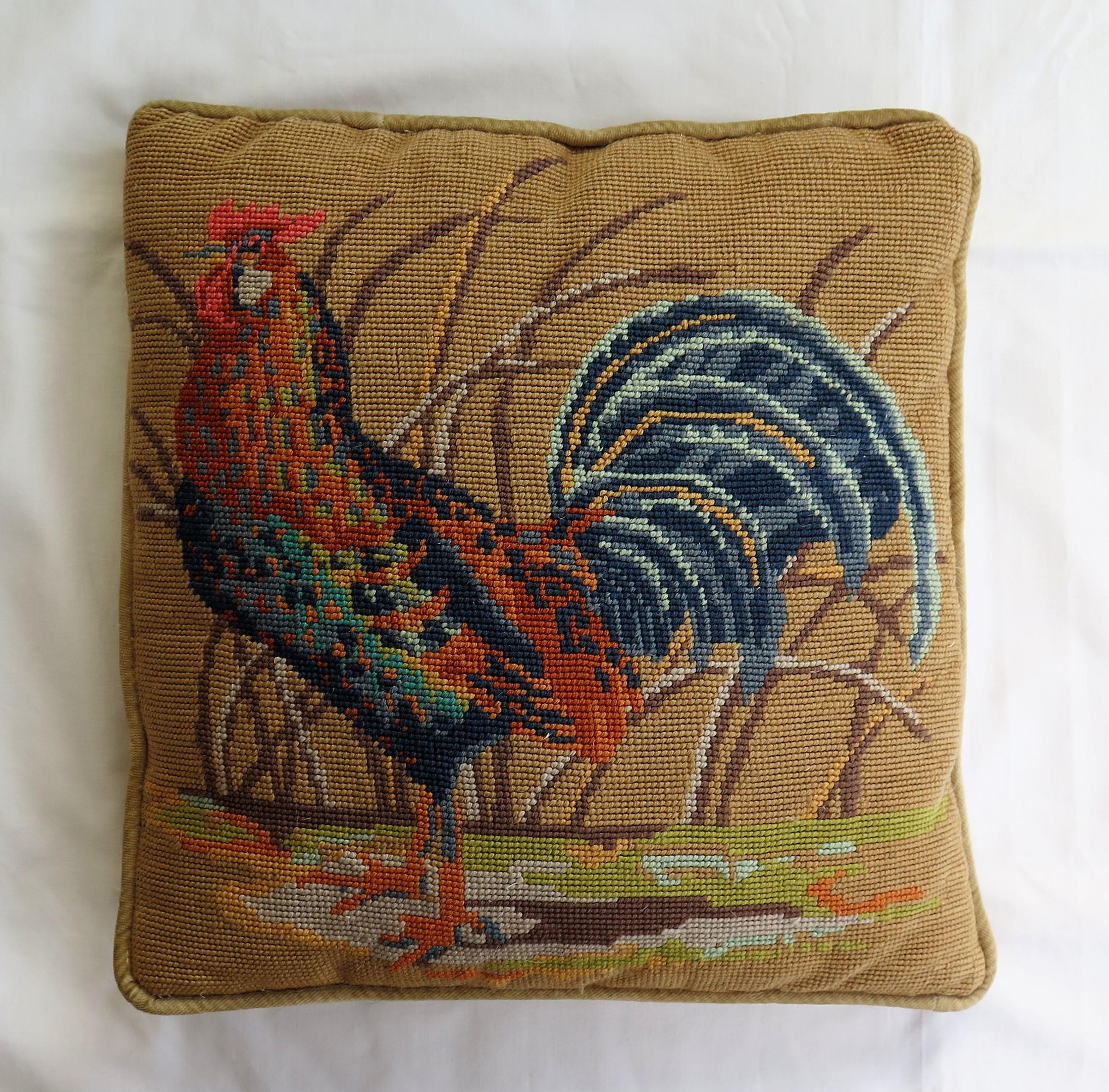 This is a mid size, English, needlepoint tapestry cushion or pillow with a distinctive country style design of a rooster or cockerel, which we date to the early or mid-20th century. 

The hand worked design shows a rooster or cockerel standing