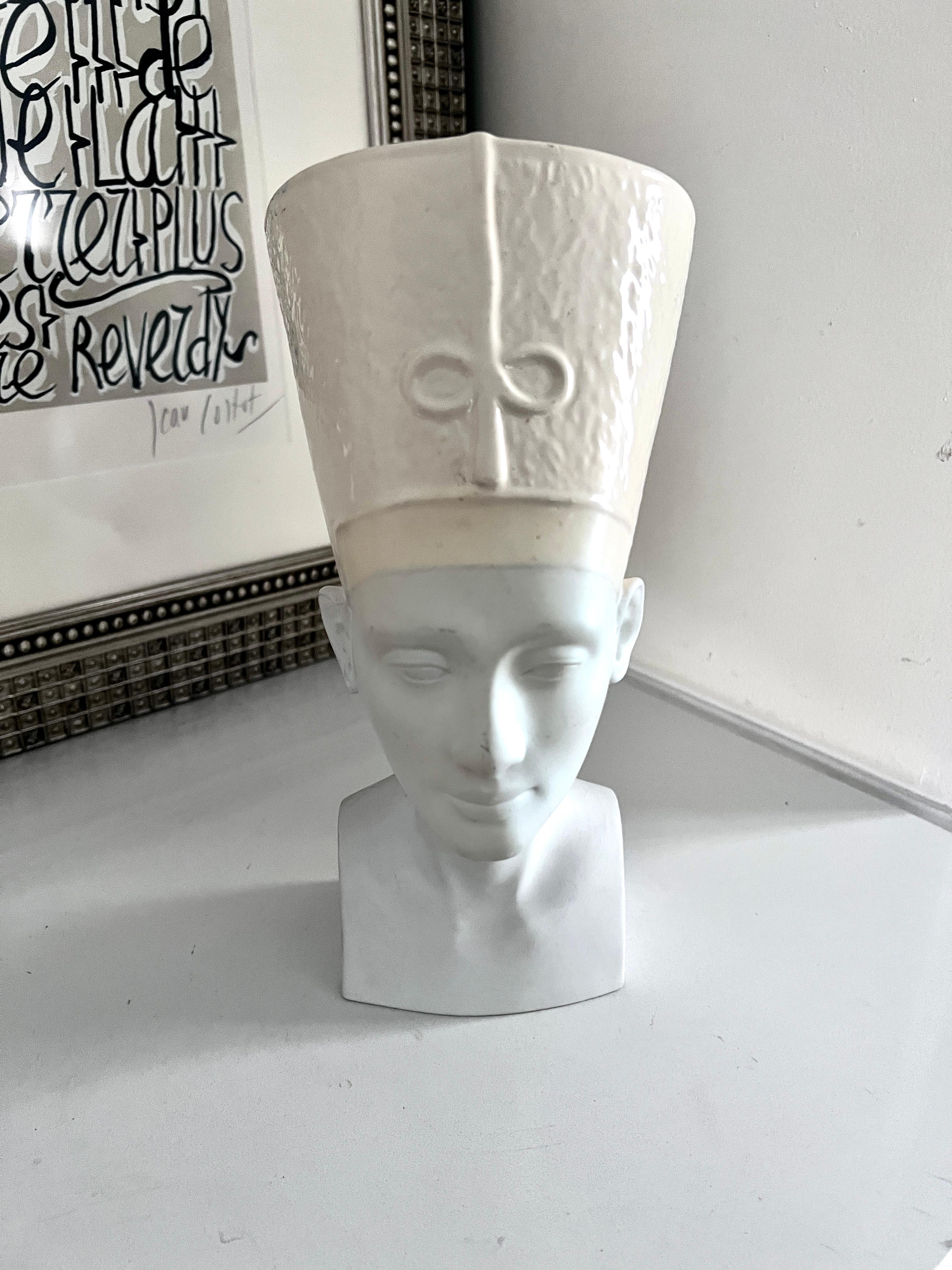 A large and beautifully sculpted head of the most beautiful woman on the Nile, Nefertiti.  

The pieces is made entirely of porcelain.  the face and neck are matte finish and white, the head dress is a bit amber and with a gloss glaze.  

A