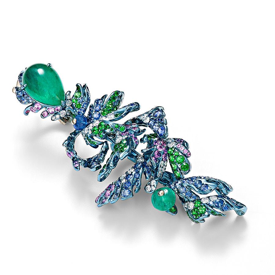 Pavona Earrings by Neha Dani are set with 9.27 Carat Emerald Pear Cabochon at the top that anchors the fluidly moving, delicate feathers of Titanium which are set with 4.30 Carat Blue Sapphires, 2.97 Carat Purple Sapphires and 3.82 Carat Tsavorite