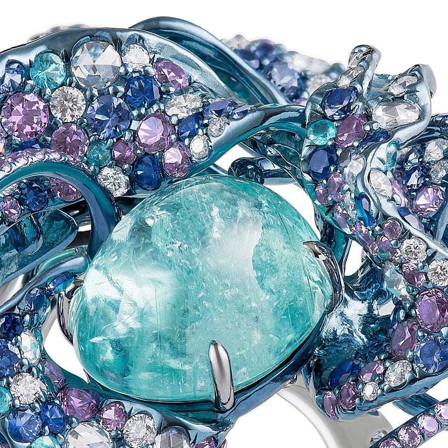 The Nuray Ring by Neha Dani has a one-of-a-kind 9.33 Carat Oval Paraiba Tourmaline Cabochon accented by 1.01 Carat Round Full Cut Diamonds, 0.71 Carat Round Rose Cut Diamonds and 0.45 Carat Paraiba Tourmalines. Blue Sapphires (2.62 Carat) and Purple
