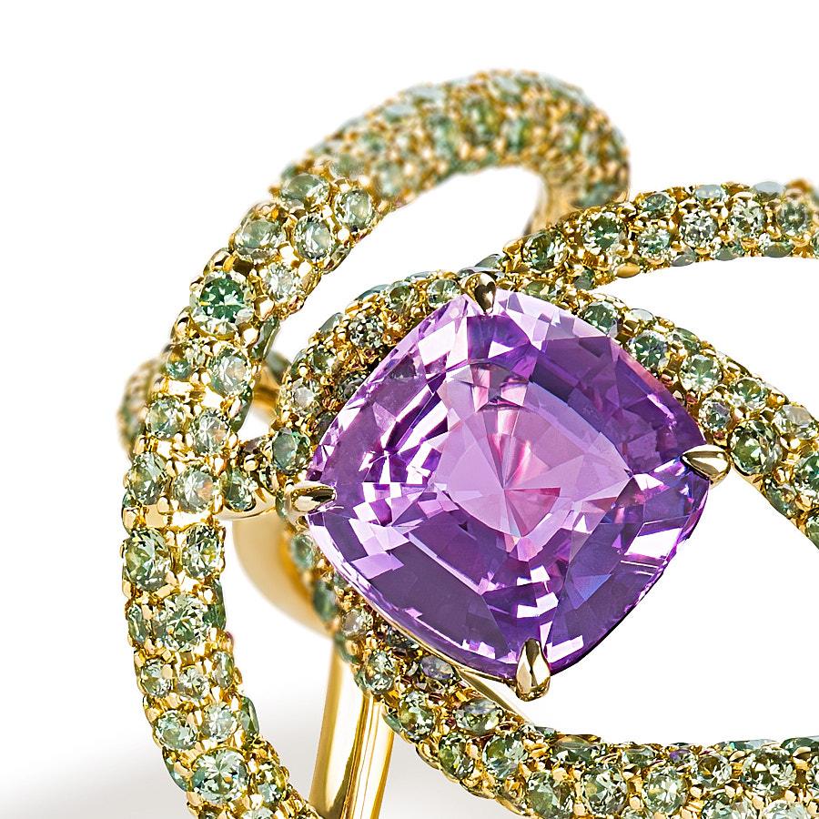 The Kephi Ring by Neha Dani resonates joy in a 4 Carat Natural Cushion Purple Sapphire, which is surrounded by 5.67 Carat Round Full Cut Green Demantoid Garnets. Set in 18K Yellow Gold, the ring is a symbol of passion.