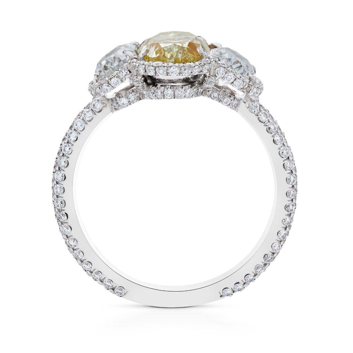 This three stone diamond ring features a central oval cut Natural Fancy Yellow diamond of 1.73 cts., flanked by two white oval cut diamonds of 1.05 cts. This notably contrasting trilogy is further accented by a diamond halo outline composed of 225