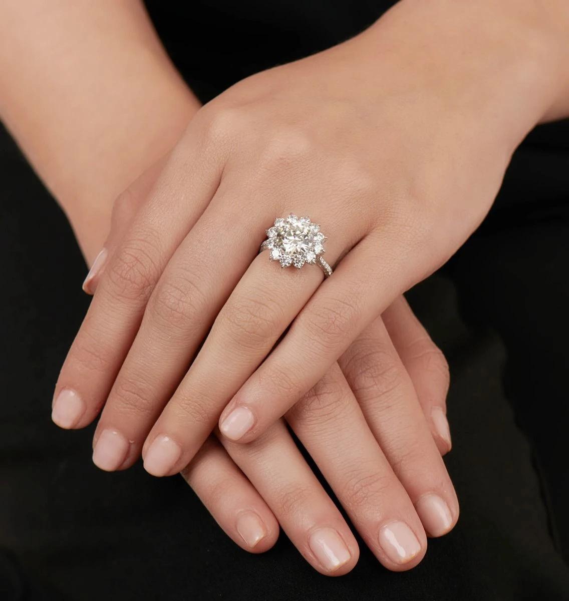 Featuring a prominent diamond sunflower arrangement, this hand made platinum ring centers upon one round brilliant-cut diamond weighing 3.01cts., set within a frame of 12 round-cut diamonds weighing 2.52 cts. Each prong evokes the appearance of a