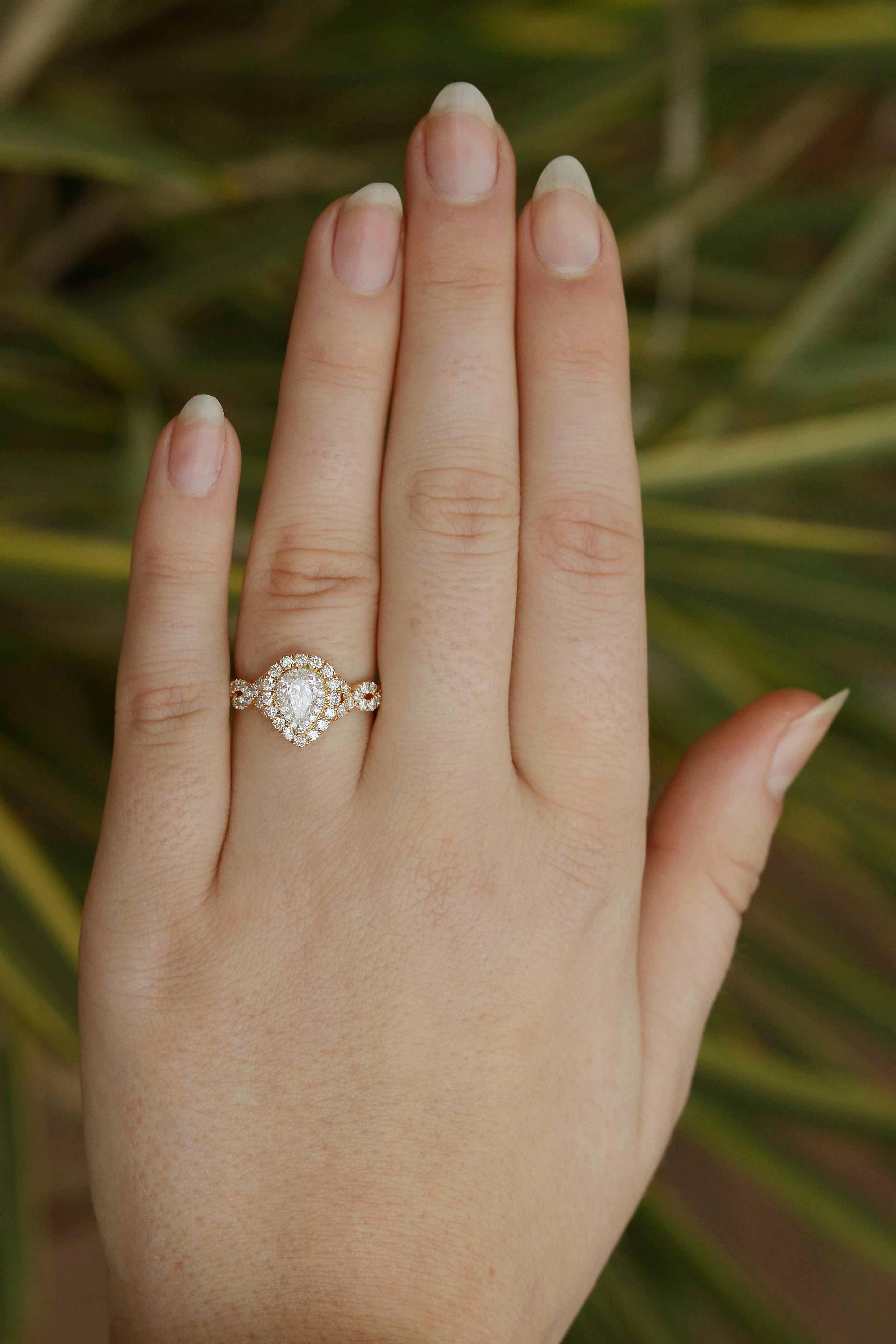 A contemporary 14k rose gold and diamond ring. The center pear-shaped diamond is dramatized by a double-halo of sparkling round diamonds and a woven infinity band studded with additional diamonds. Stamped with well-known designer 