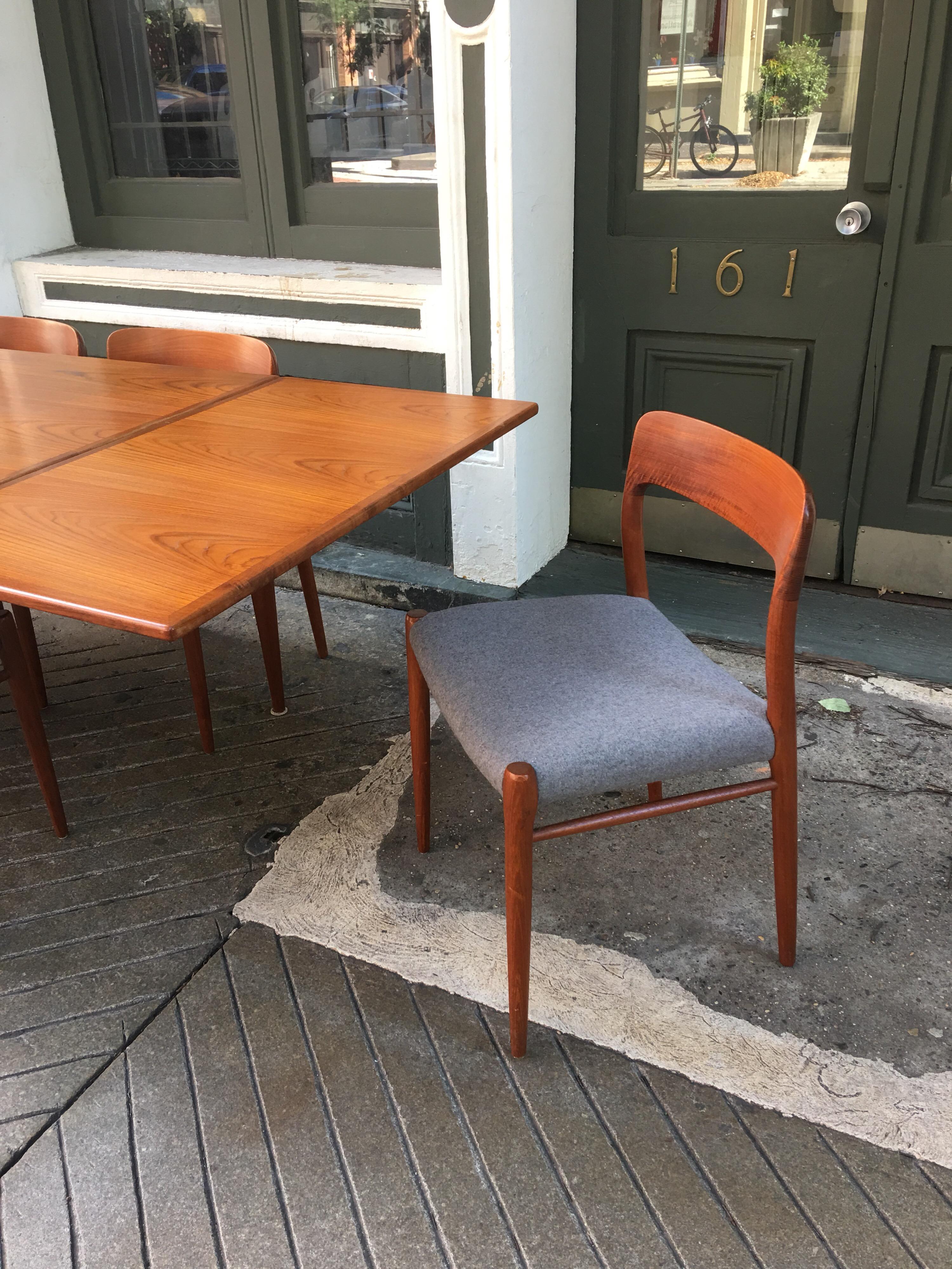 Neils Moeller teak dining table and six chairs with metal enameled label on table. Chairs were recently redone in a medium gray tightly woven wool fabric. Table has two refractory leaves at either end adding another 42 inches to the length of the