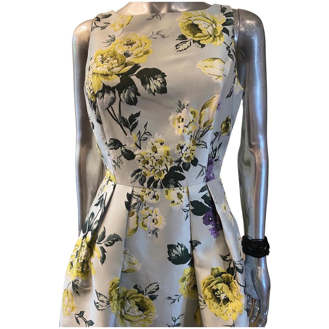 The perfect dress to wear for a summer wedding. A lovely muted light grey ground with lemon and violet colored floral jacquard fabric made by Neiman Marcus. Sleeveless bodice with flared skirt. The skirt is beautifully pleaded at the waist front and