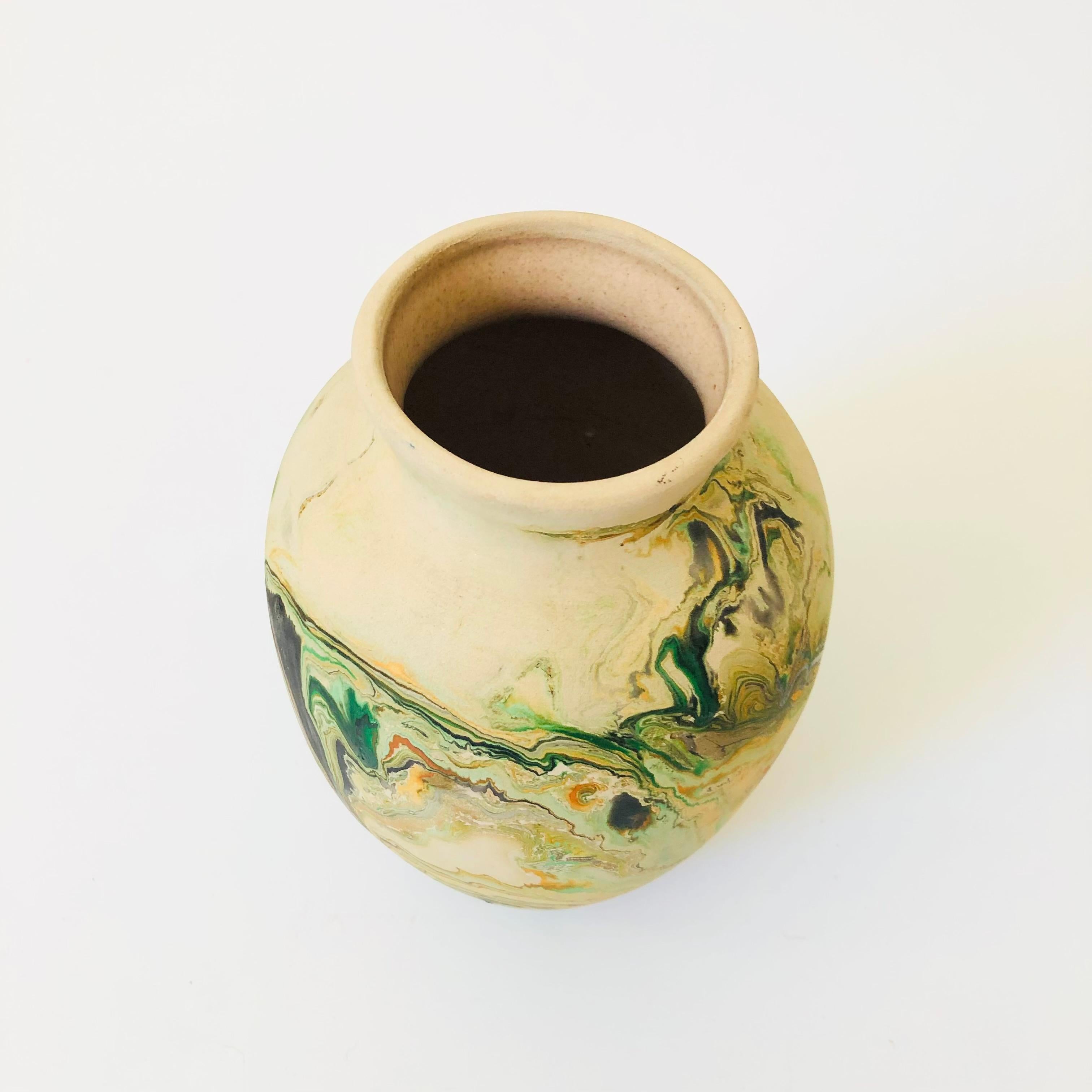 A vintage nemadji pottery vase with a beautiful organic pattern of green and orange swirls on a light off-white background, matte glaze. Glazed interior.

