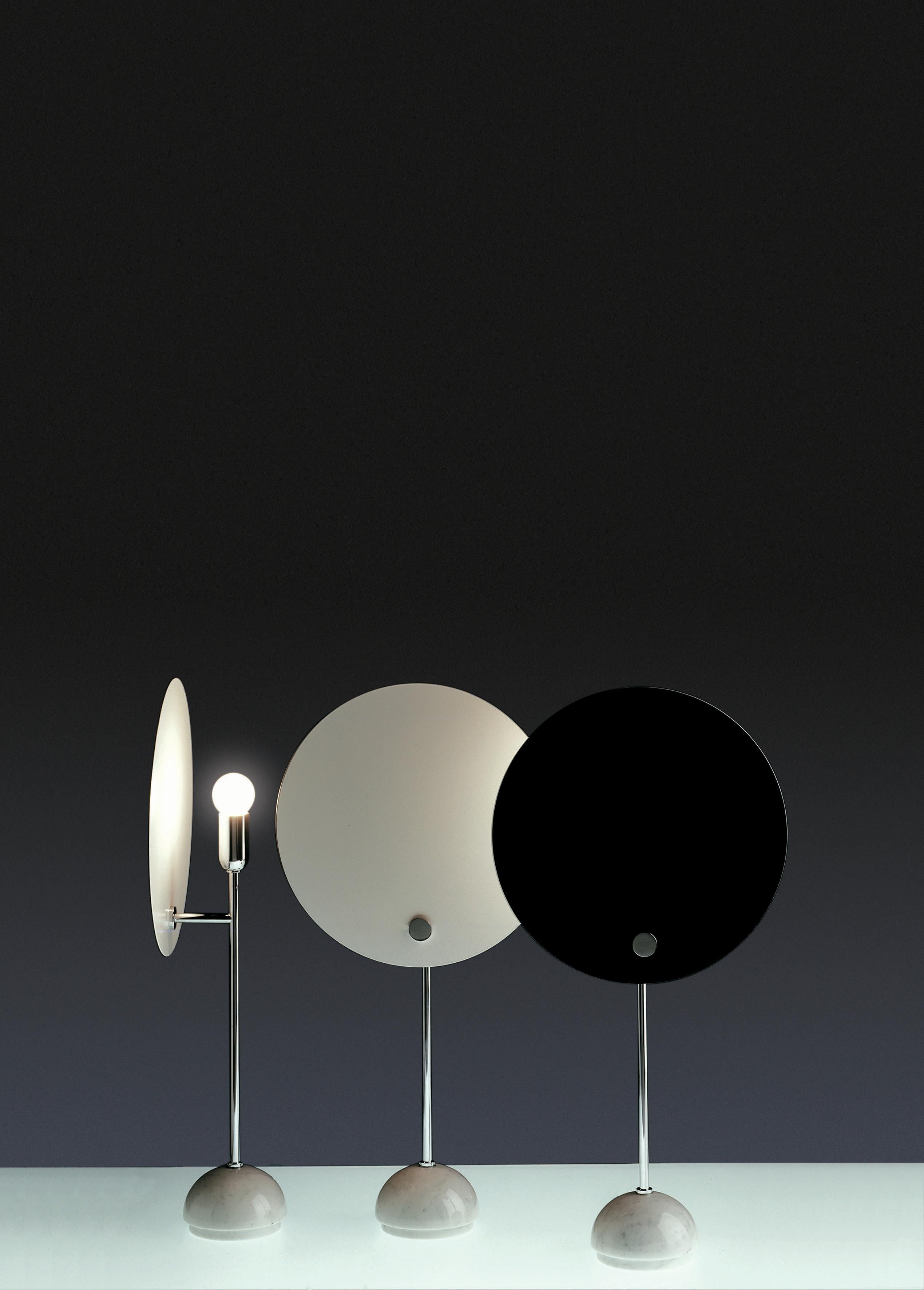 Lampe de table dotée d'un réflecteur circulaire en aluminium qui masque la répartition de l'éclairage, donnant l'effet d'une éclipse solaire. L'écran circulaire est peint en blanc et noir, la tige et les petites pièces métalliques ainsi que le