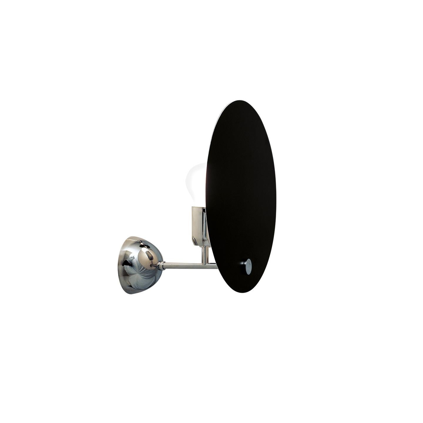 Lámpara de pared con un reflector circular de aluminio que apantalla la distribución de la luz, dando el efecto de un eclipse solar. La pantalla circular está pintada en blanco y negro, el vástago y las piezas pequeñas de metal y el soporte