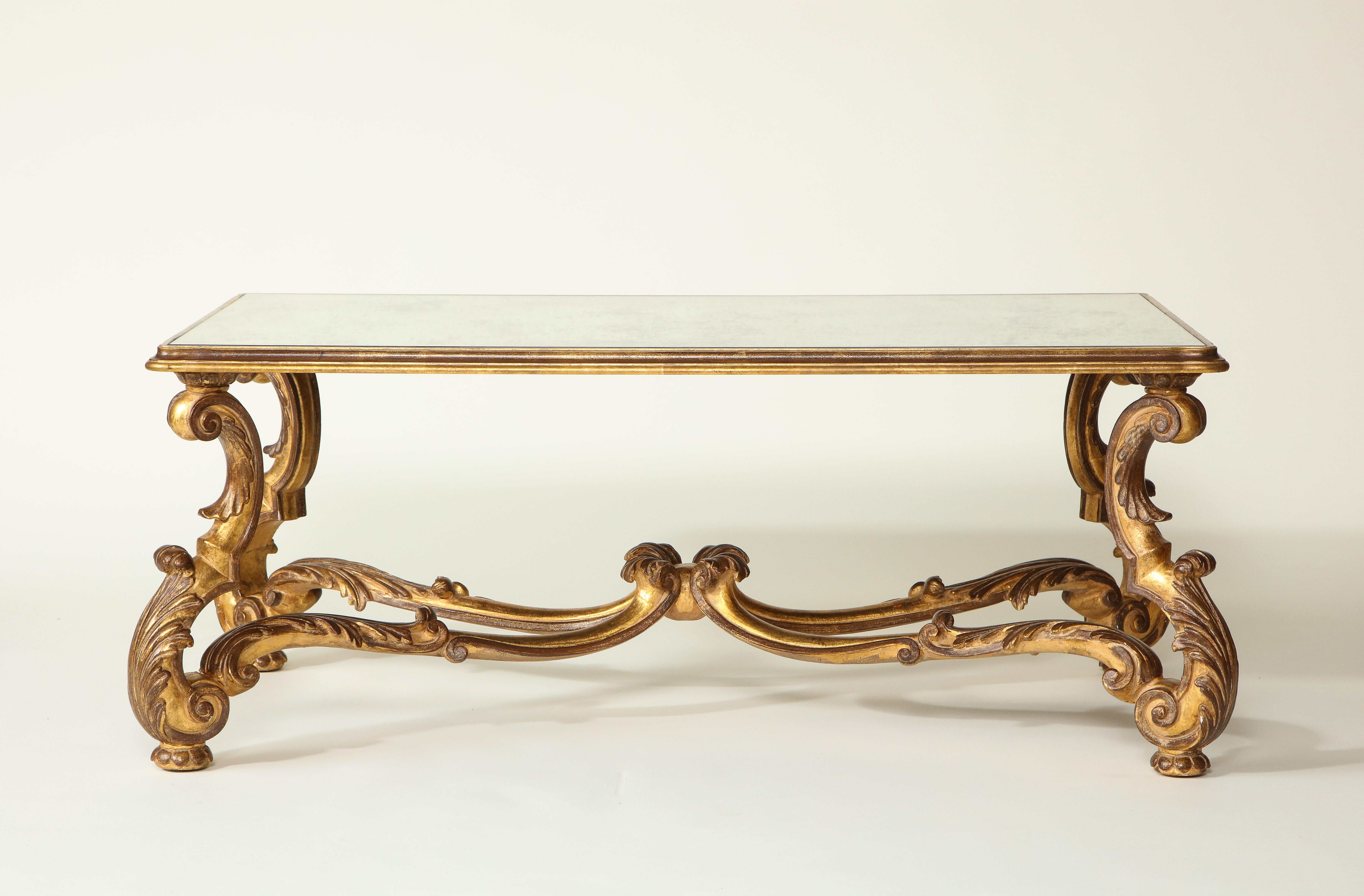 The rectangular top inset with an antiqued mirror plate; raised on acanthus-leaf carved volute supports joined by an arched scroll-form stretcher.