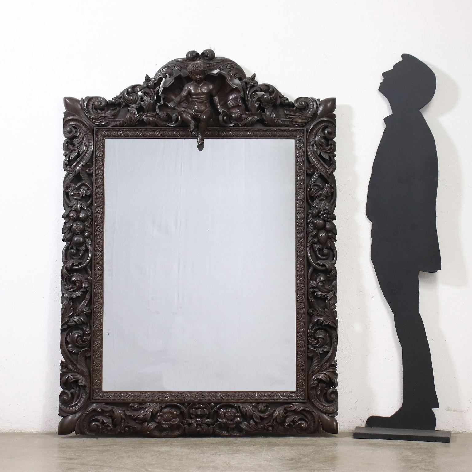 Neo-Baroque mirror, entirely carved with leafy volutes, with a shell and a putto on the frame; oak.