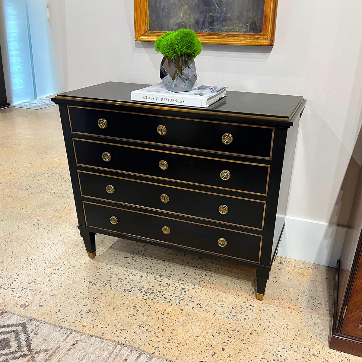 The four-drawer chest is beautifully lacquered and ebonized with a high sheen. The rectangular top and drawer fronts are framed with solid brass trim and the drawers have traditional-style brass ring pull handles. 

Raised on square tapered feet