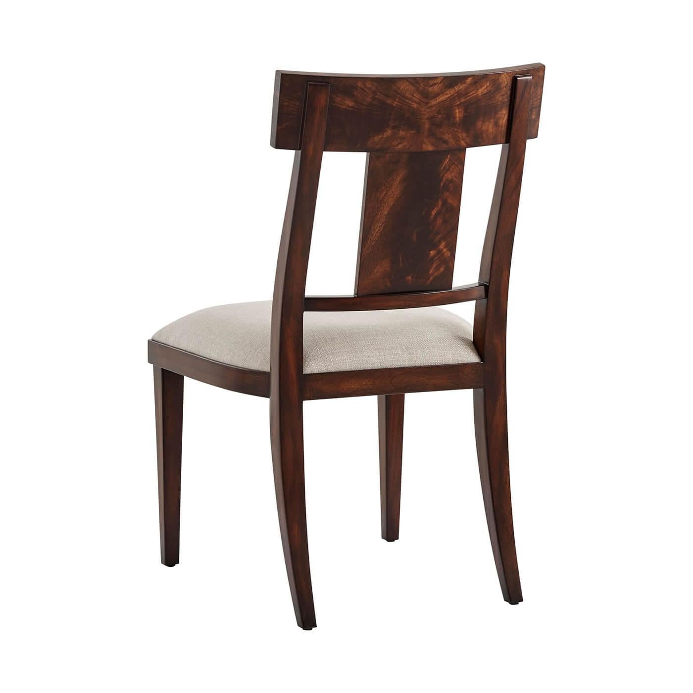 Moderner Beistellstuhl aus Mahagoni im Neoklassizismus, mit flammenfurnierter Stangenschiene und massiver Leiste über einem gepolsterten Sitz, auf quadratischen, spitz zulaufenden Beinen.
Abmessungen: 20