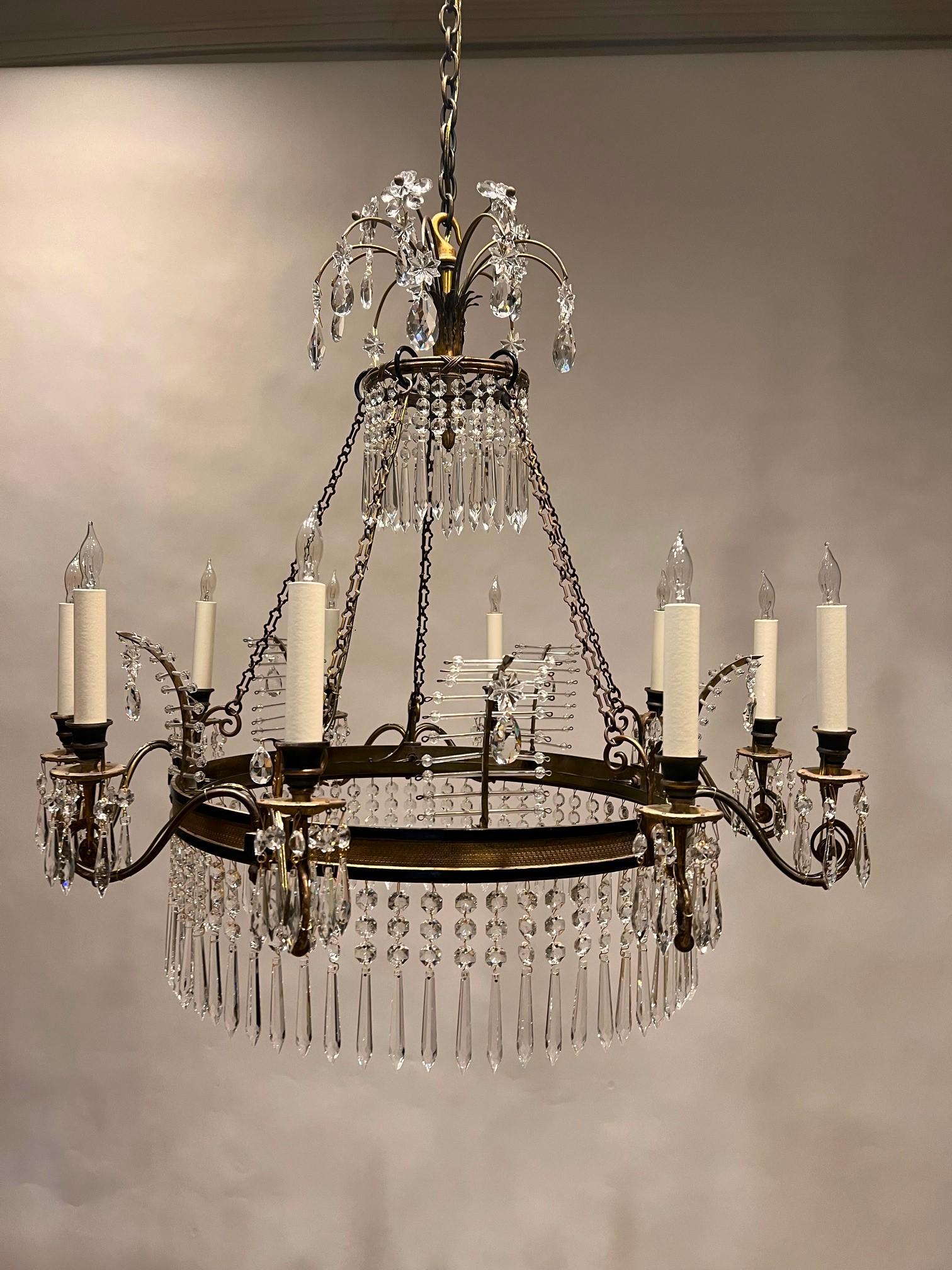 This elegant Neo-Classic 10-light chandelier, though made in Italy, is inspired by Regency England. The bronze and patinated bronze frame was put together from hand-cast components. 
The hand-cut prisms are French.  The floral crown, crystal fern