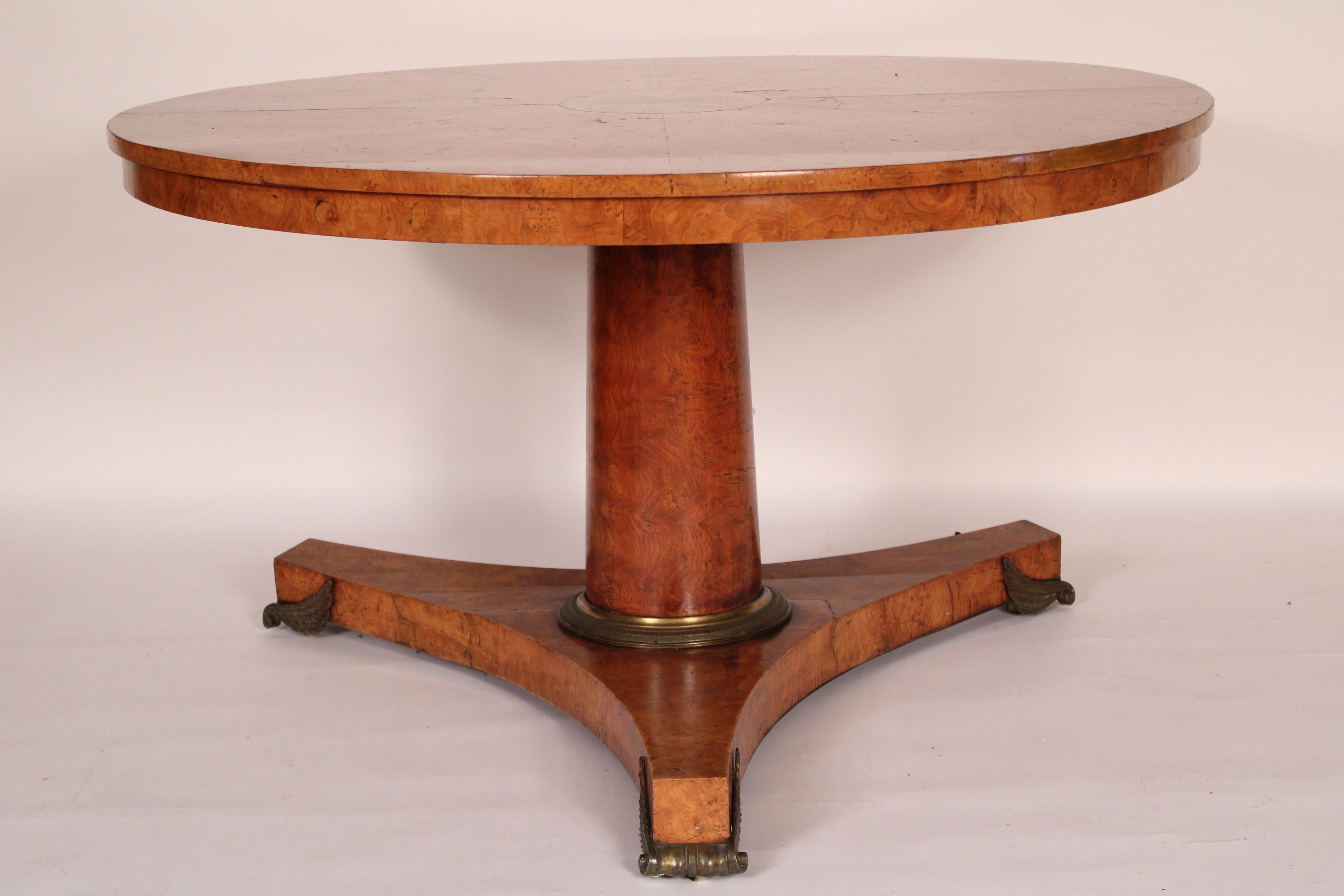 Continental neo classical burl ash center table, circa 1830. With a round burl ash top, a tapering central column with a bronze ring at the base, a tri form platform base, resting on bronze feet. 