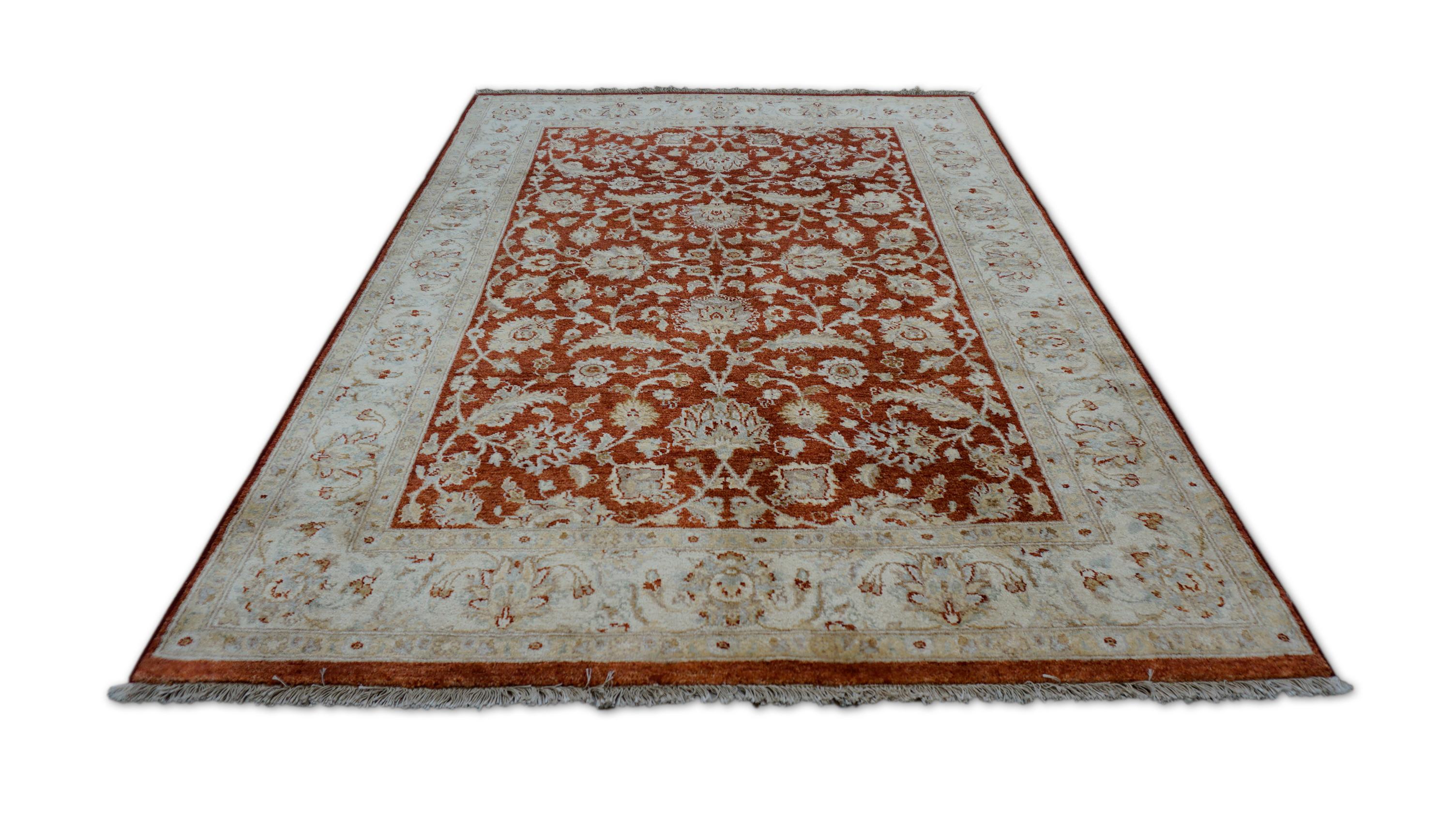 Ce tapis en laine noué à la main met en valeur la beauté durable de l'art floral d'inspiration moghole. Rendu dans un chaud champ rouge rouille, le tapis présente un motif complexe de palmettes, de gerbes florales et de rinceaux de vigne,