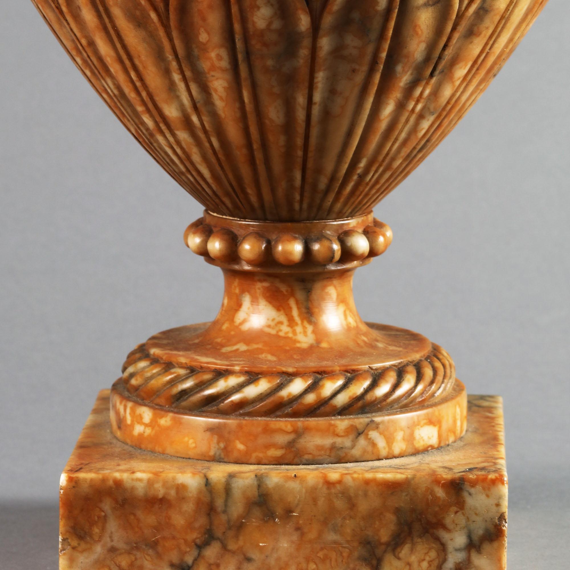 A fine neoclassical urn in carved alabaster, the richly figured stone reminiscent of fine Siena marble, the figuratively carved lid with gadrooning, supported on a waisted neck and bulbous body, the shoulders and base with overlapping leaves.
