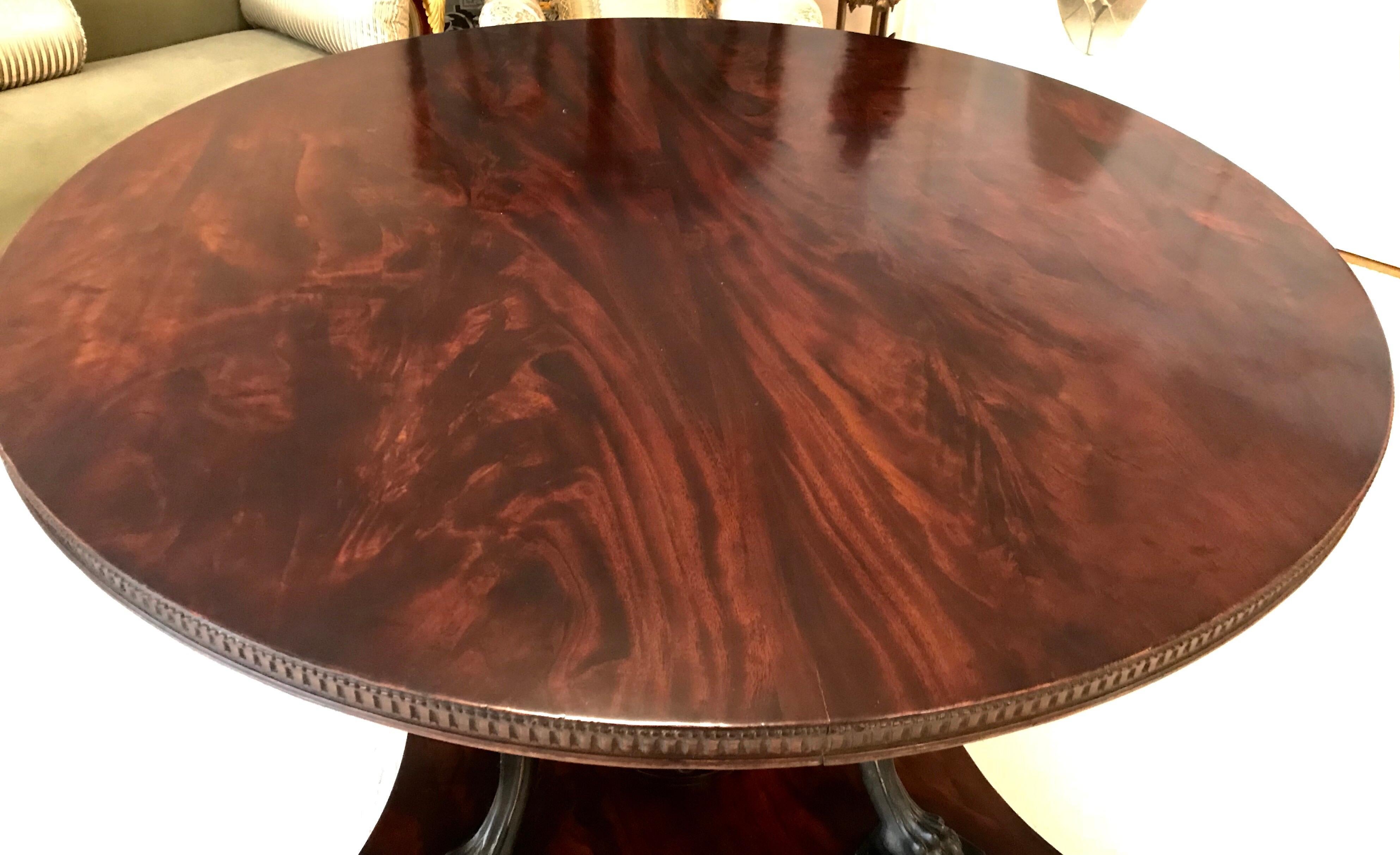 This stunning English neoclassical center table has a platform base with a central shaft and four hand carved ebonized winged Griffins holding the highly figured mahogany top. The carving is masterfully done and has some gilded highlights.