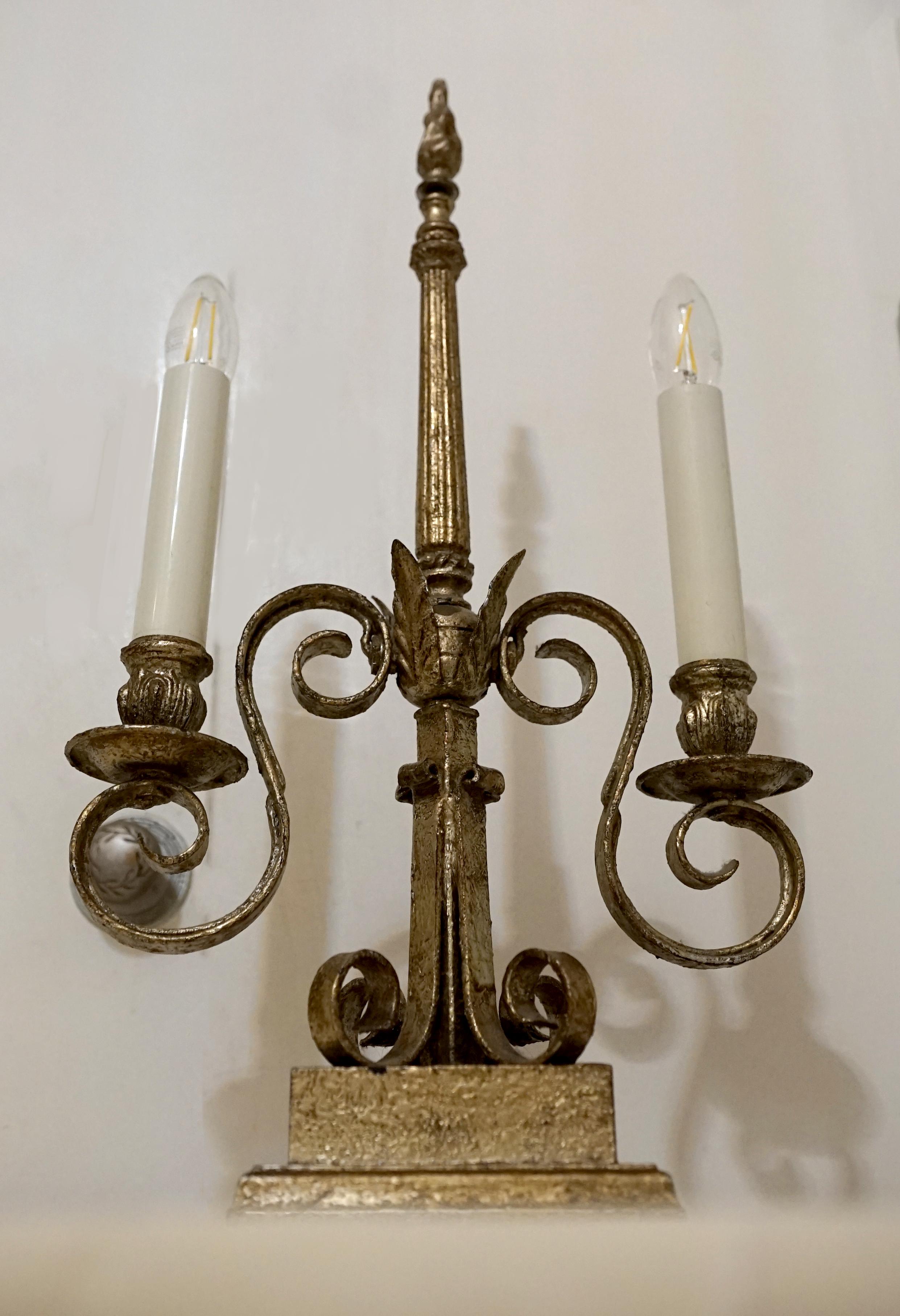 A beautiful two-light candelabra makes for perfect statement lighting. This lamp was produced circa 1925 to 1950, and it exudes design chic and grace. This is a heavy piece that includes iron scrolls and brass elements in a size that is not too big
