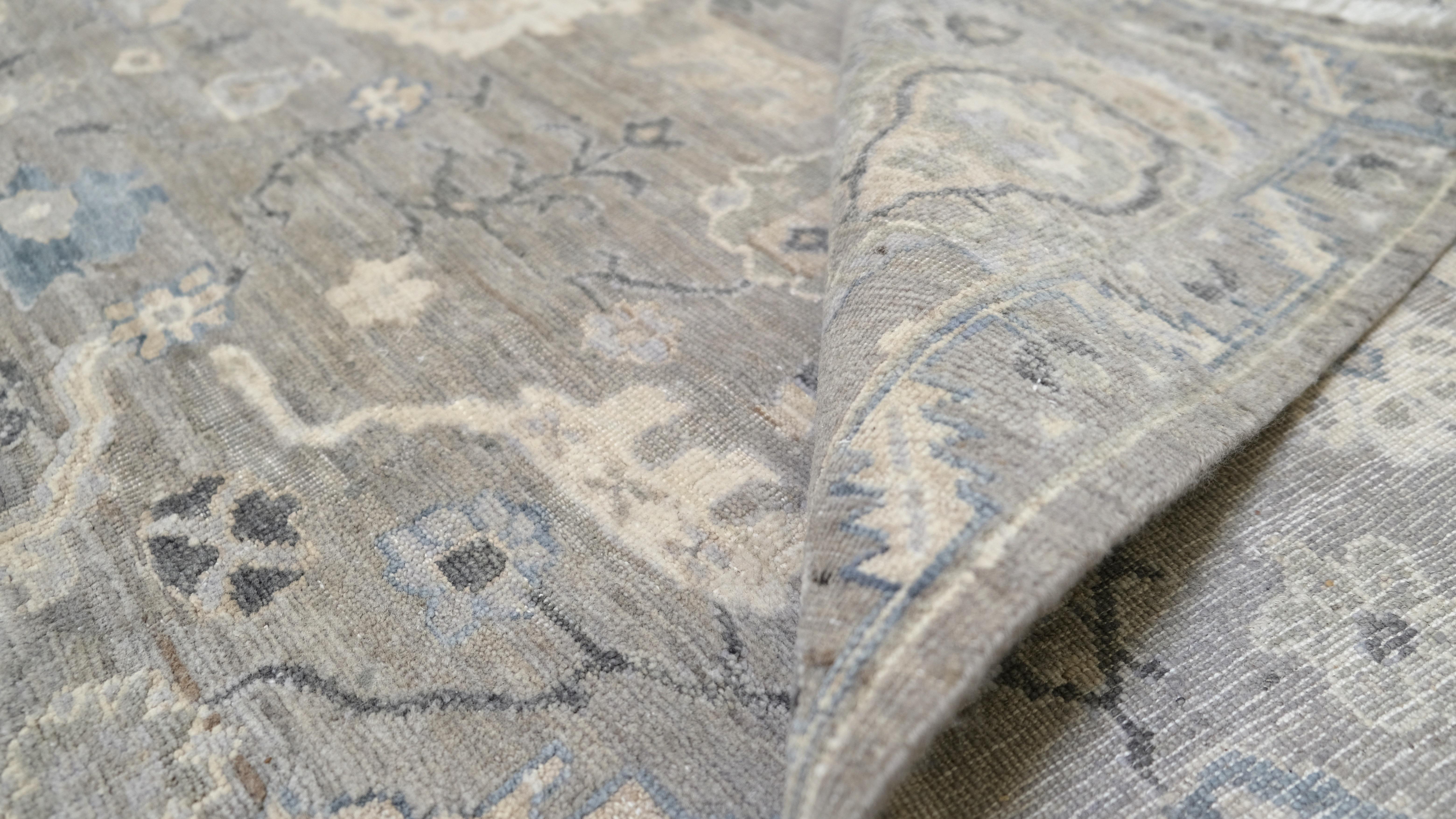 Dieser exquisite, handgeknüpfte Wollteppich zeigt eine raffinierte Mischung aus weichen Grau-, Elfenbein- und gedämpften Blautönen, die eine zeitlose und dennoch moderne Ästhetik schaffen. Inspiriert von klassischen Designs, zeigt der Teppich ein
