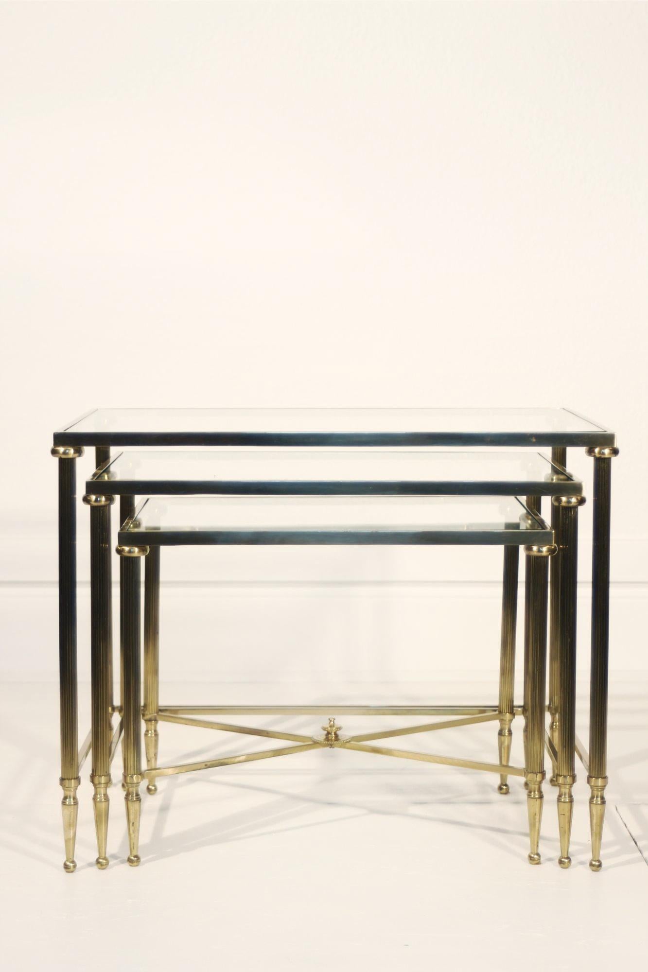 Mid-century nesting tables in gilded brass and tempered glass, attributed to the famous French furniture maker Maison Jansen, known for making high quality pieces of furniture popular in Parisian interiors of the time. 

The design is typical of the