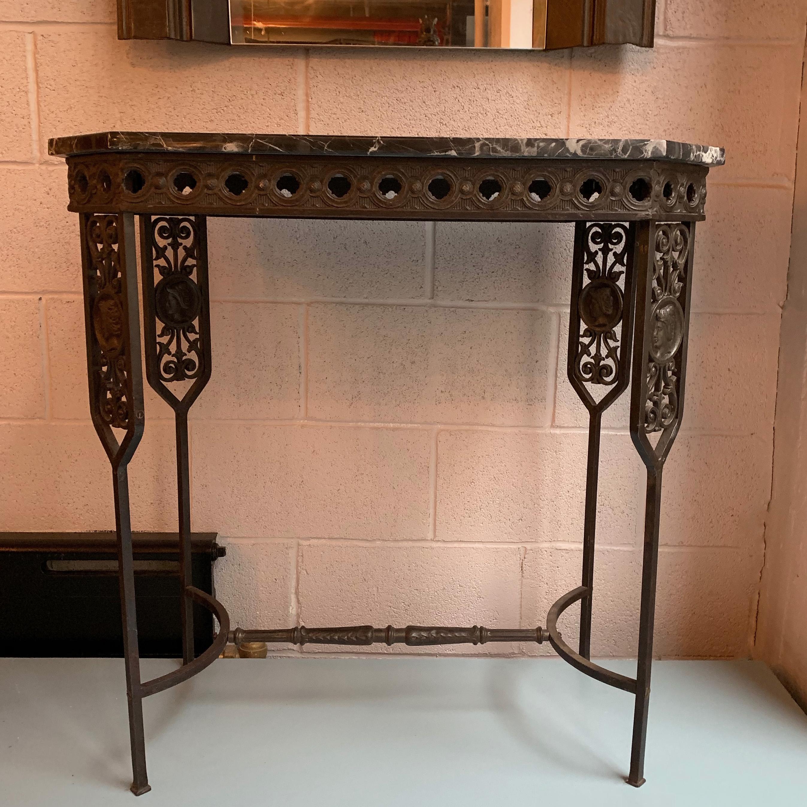 Neoclassical revival, console table, circa 1920s features a decorative wrought iron base with cast iron medallions and a wonderfully grained black marble console table. Two tables are available.