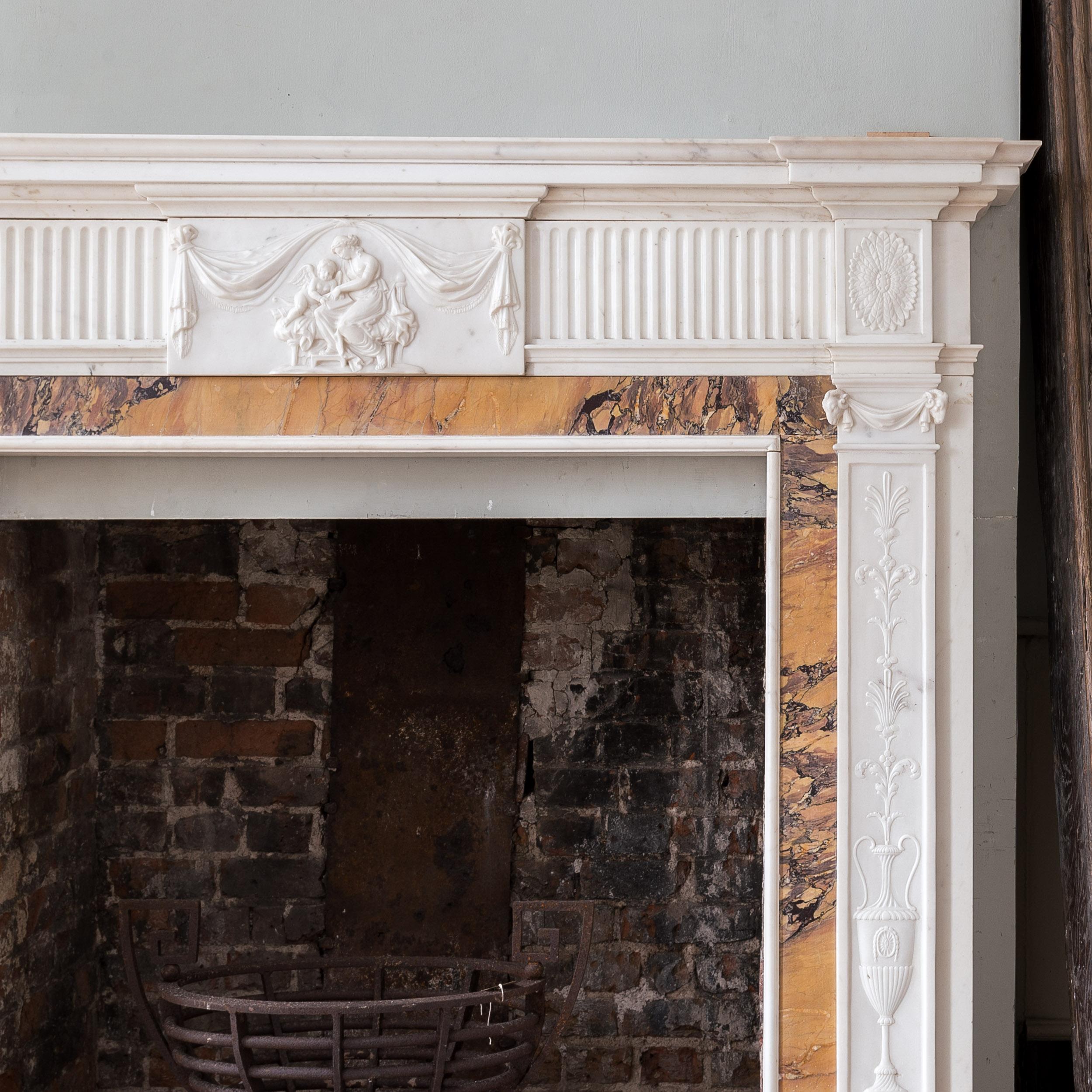 Nineteenth century neo-classical fireplace in the George III style, the stepped shelf above fluted frieze centred by plaque carved in relief depciting Cupid with a maiden, the foliate oval paterae corner blocks above pilaster jambs of classical urns