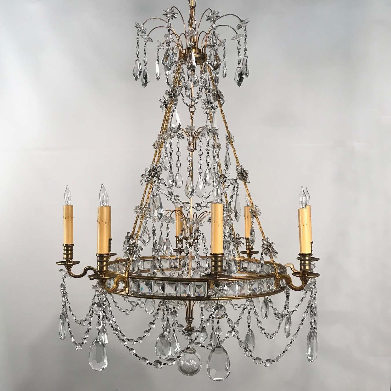 This is a most unusual chandelier. The central band is set with square faceted prisms and supports eight arms, now electrified. There is a considerable variety of quality crystals, some of flower- head-form, some Swedish pendalogues, some garlands.