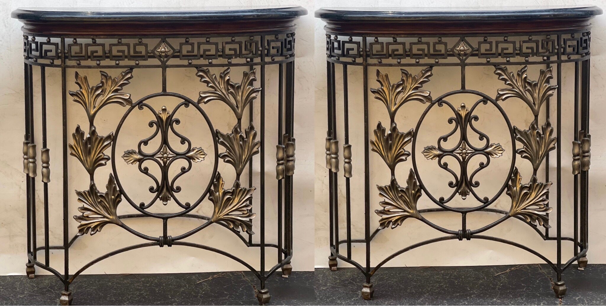 I love these! This is a pair of iron consoles with a black tessellated marble on a mahogany top. The iron base has a wonderful Greek key banding and bronze foliate accents. They are in very good condition and are unmarked.